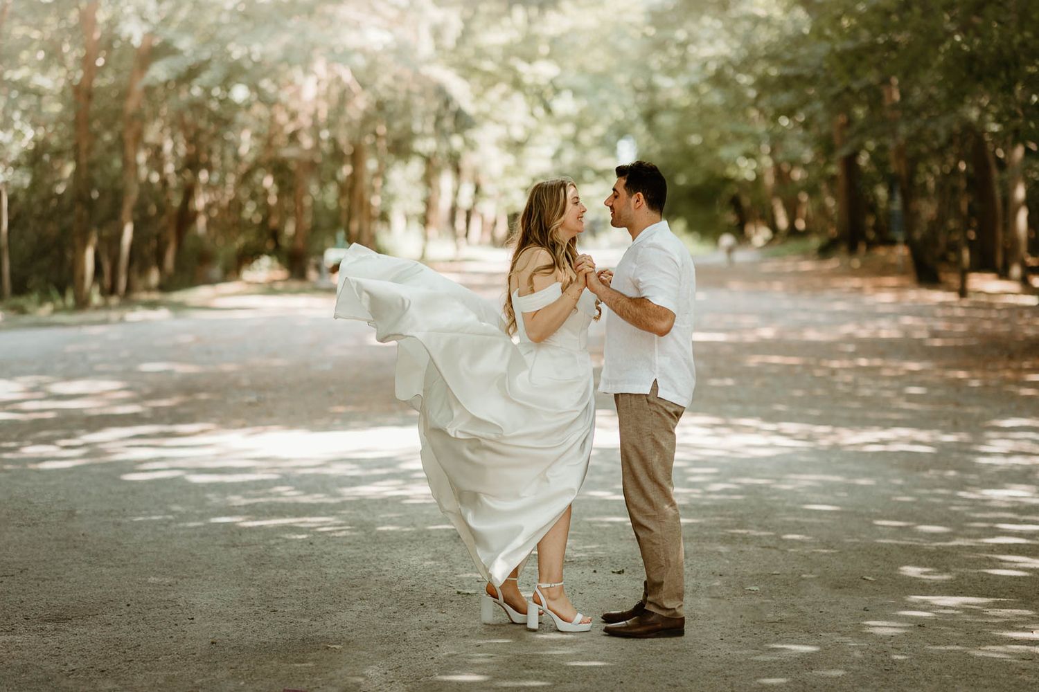 A couple dances together in a sunlit wooded area during their wedding photoshoot.