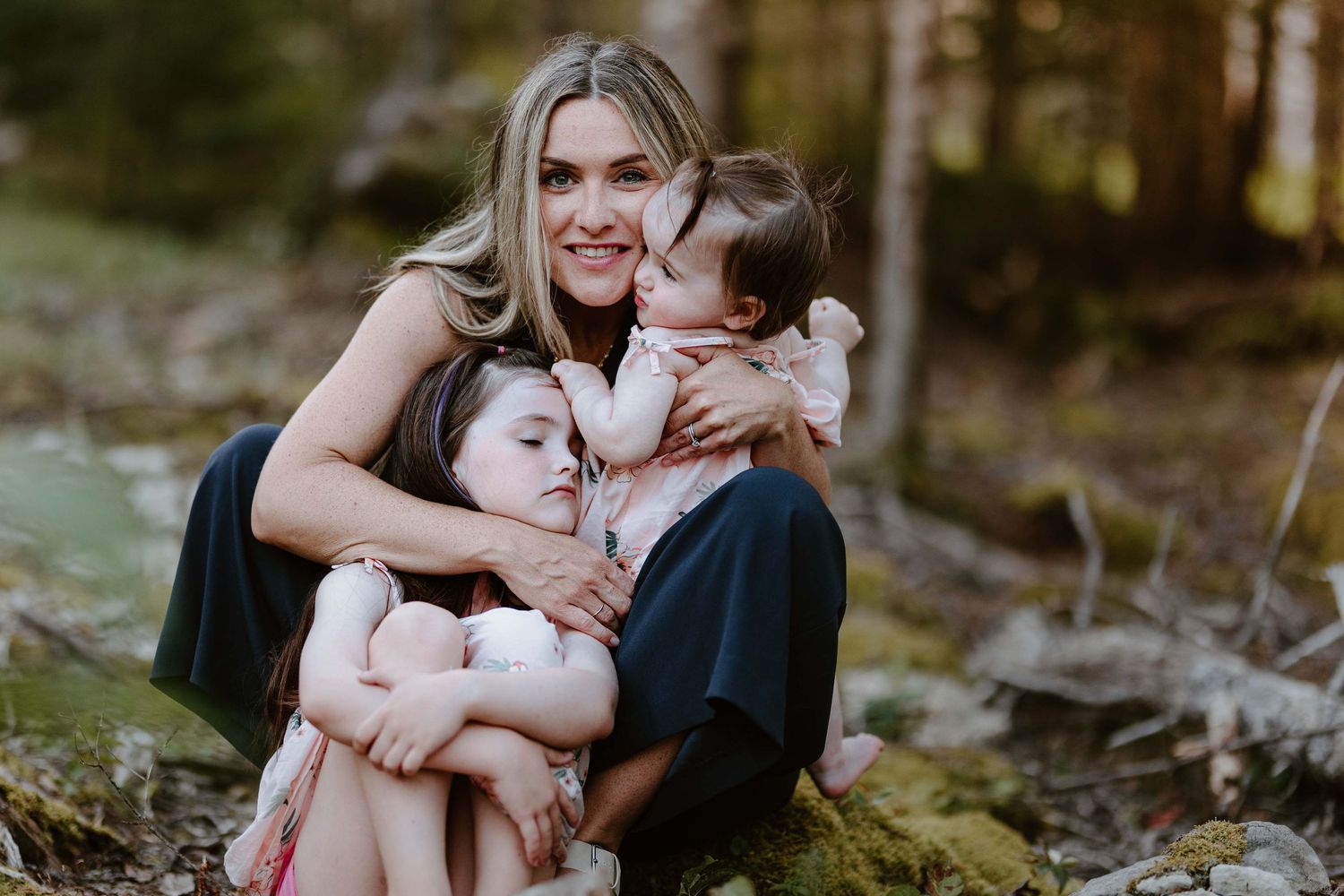Family embracing together on mossy ground in forest setting.