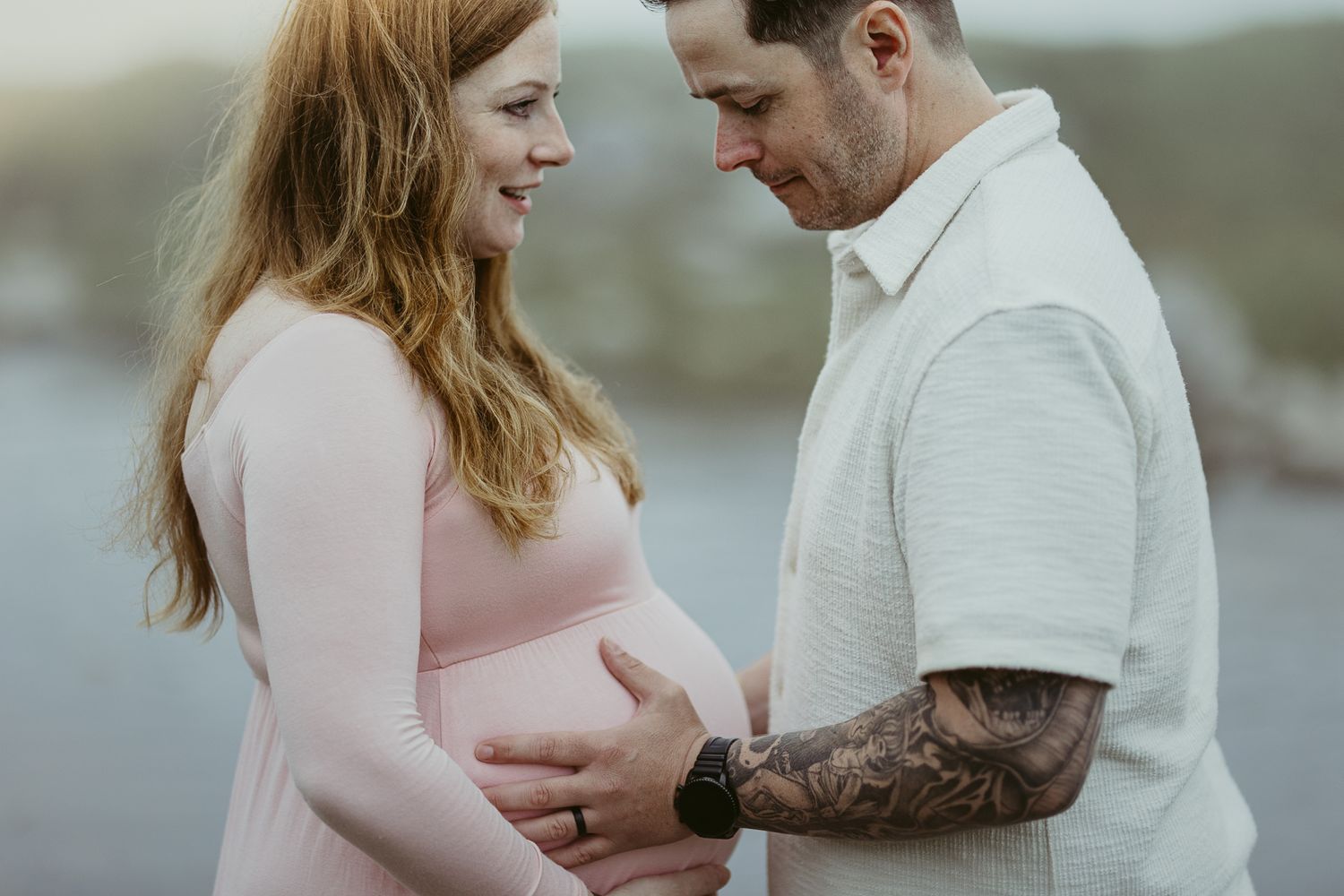 Intimate maternity portrait with couple in pink and white against moody backdrop.