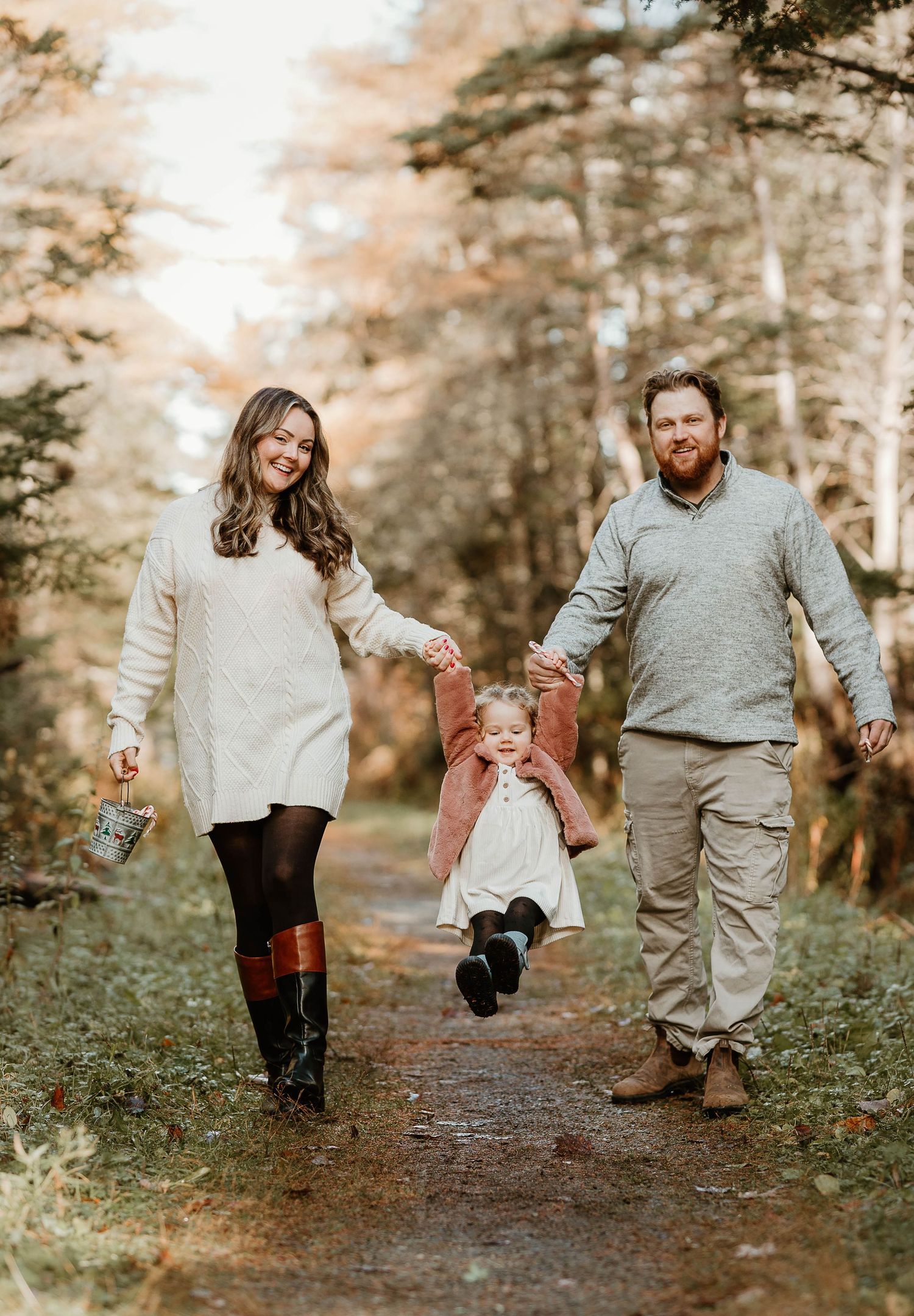 Family of three walking on a forest path in autumn, swinging their young child between them.