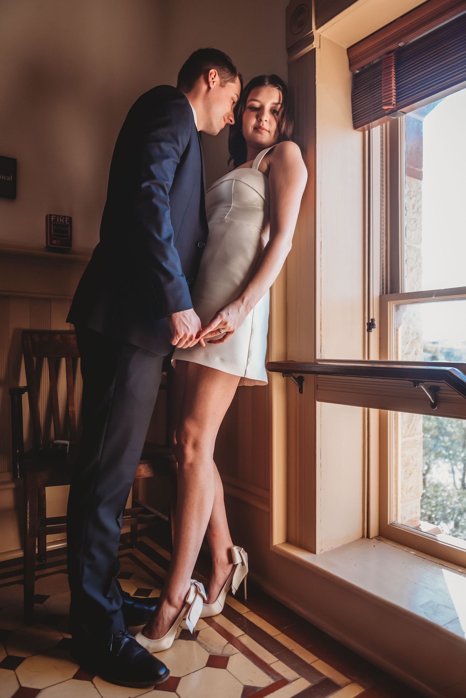 A couple shares an intimate moment by a window in a rustic wooden interior with warm lighting.