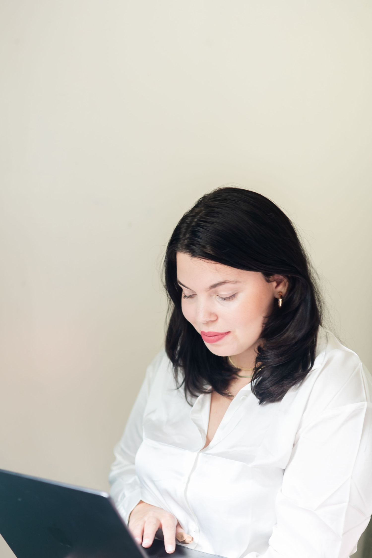 A woman in a white button-down shirt works intently at a desk in a minimalist setting.