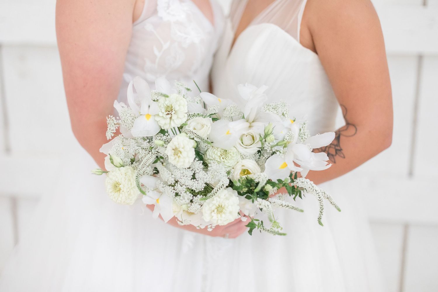 White bridal bouquet with delicate flowers and greenery against light background.