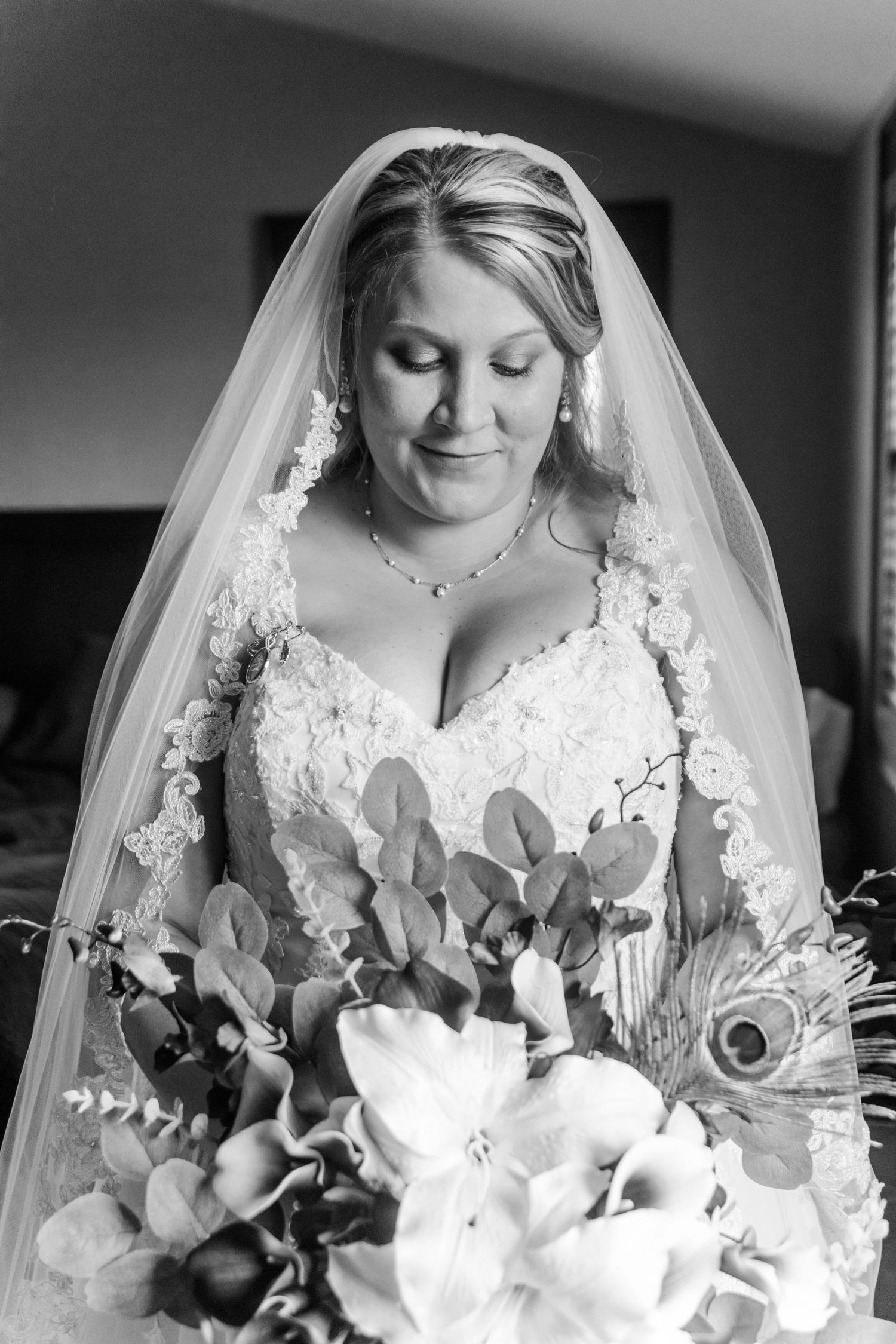 Elegant bridal portrait with lace veil and white floral bouquet in black and white.