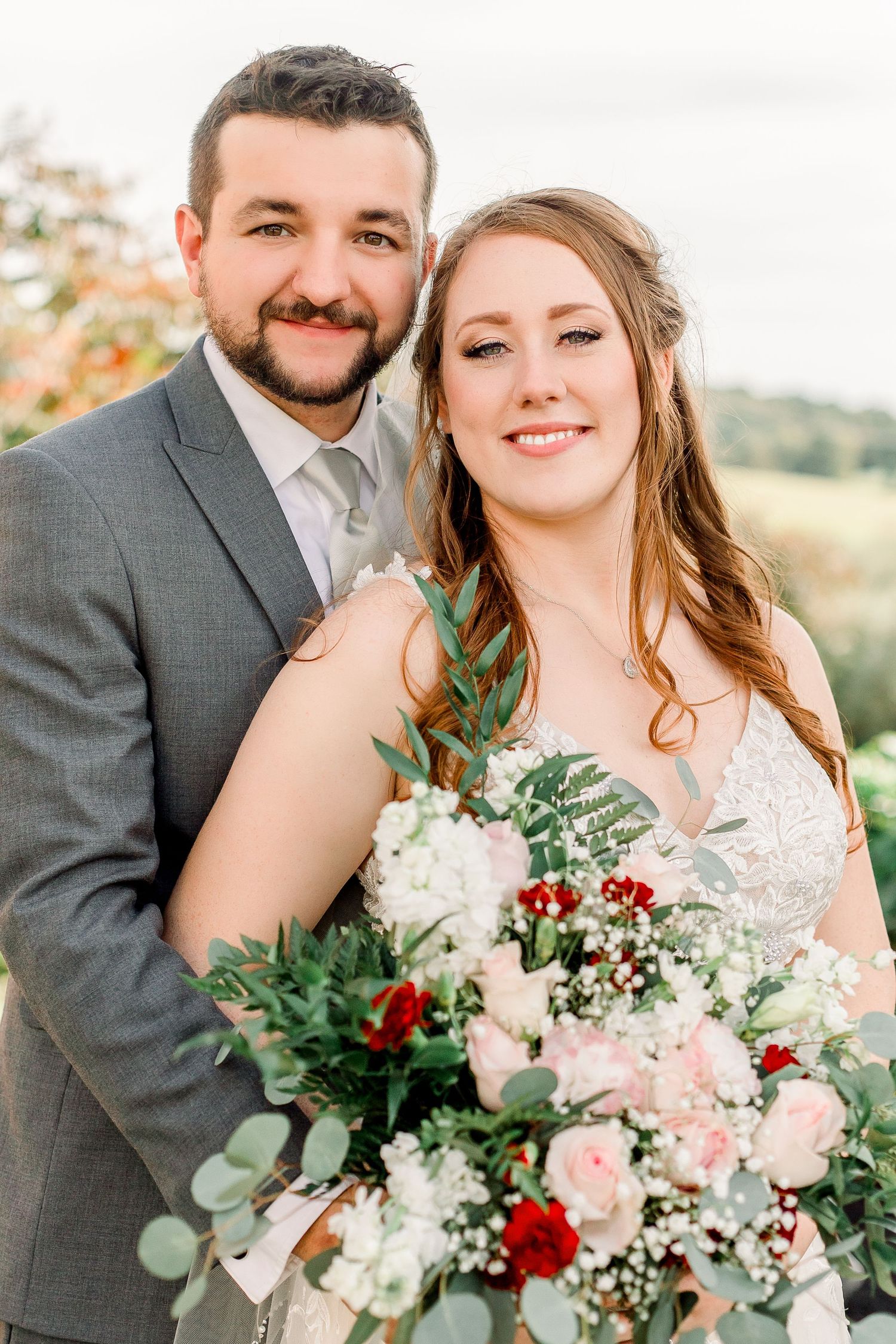 Wedding couple poses with beautiful bouquet featuring red and white flowers with eucalyptus greenery.