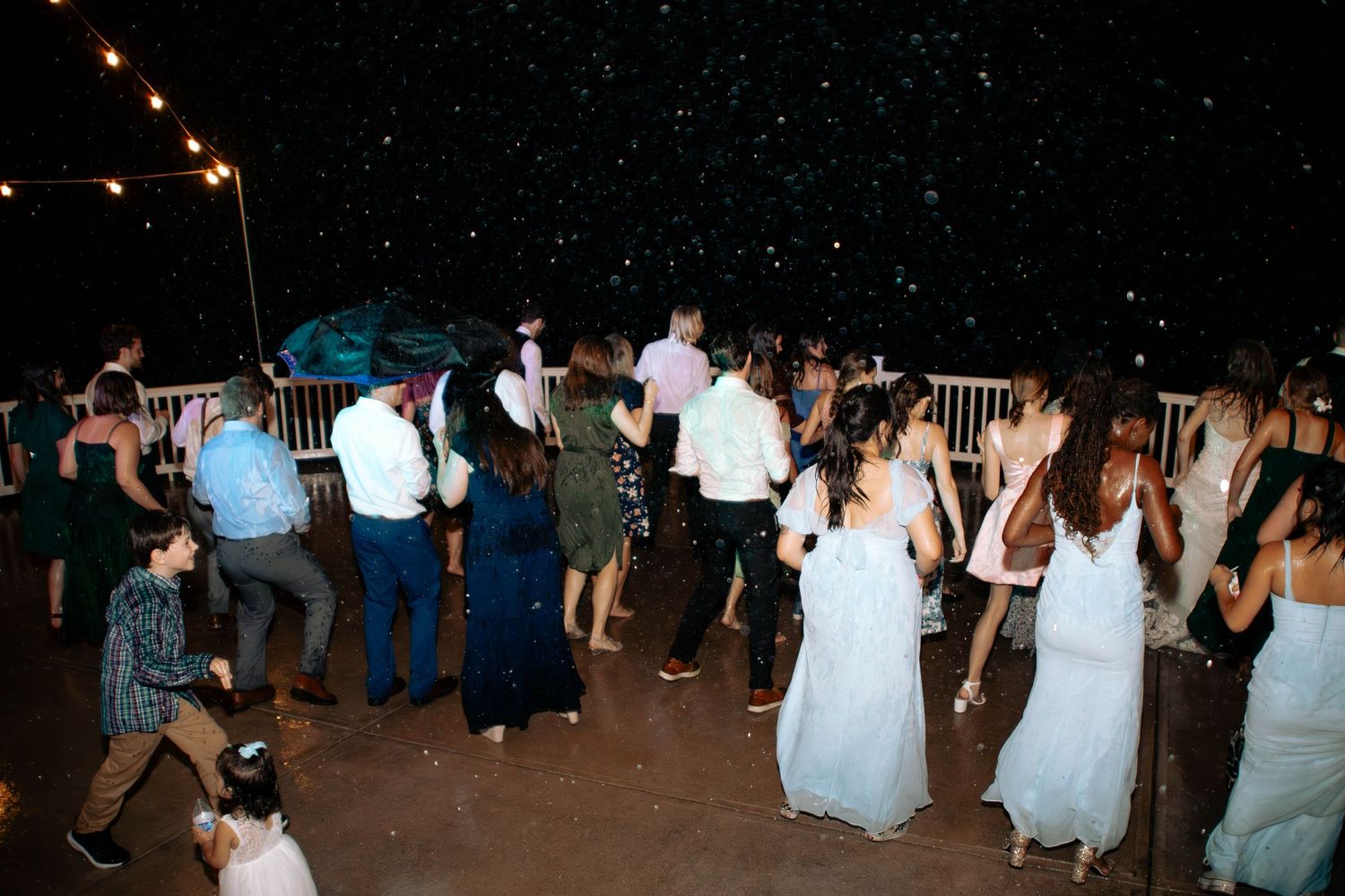 People dancing at a nighttime outdoor wedding reception with string lights illuminating the wooden deck area.