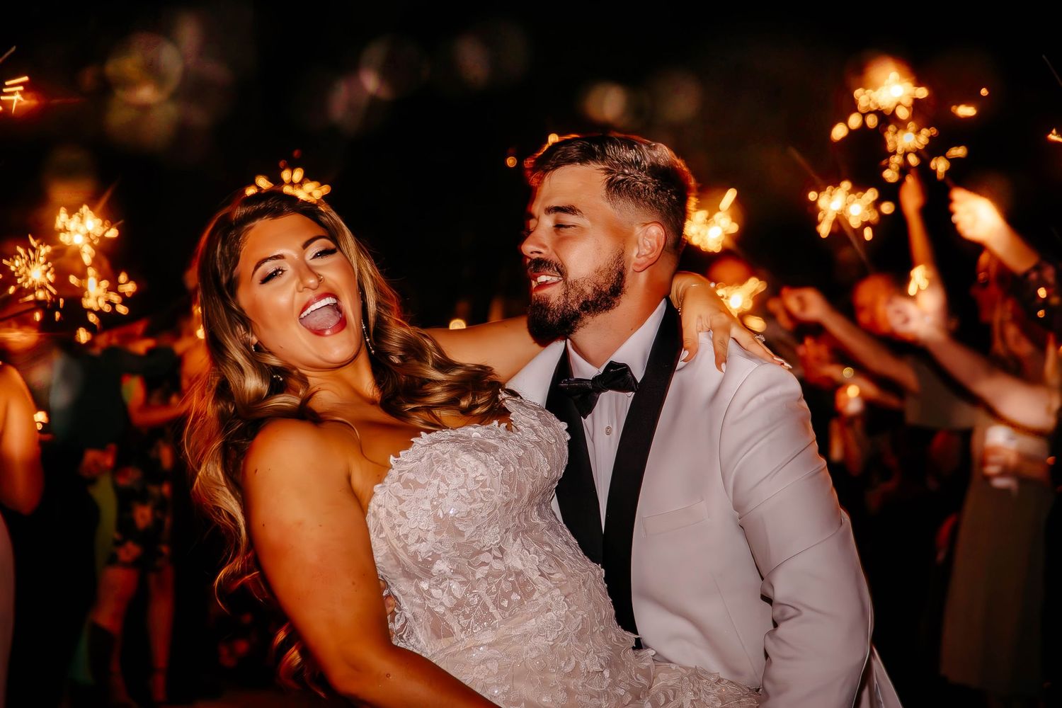 A couple celebrates at their wedding reception with sparklers glowing warmly in the night background.