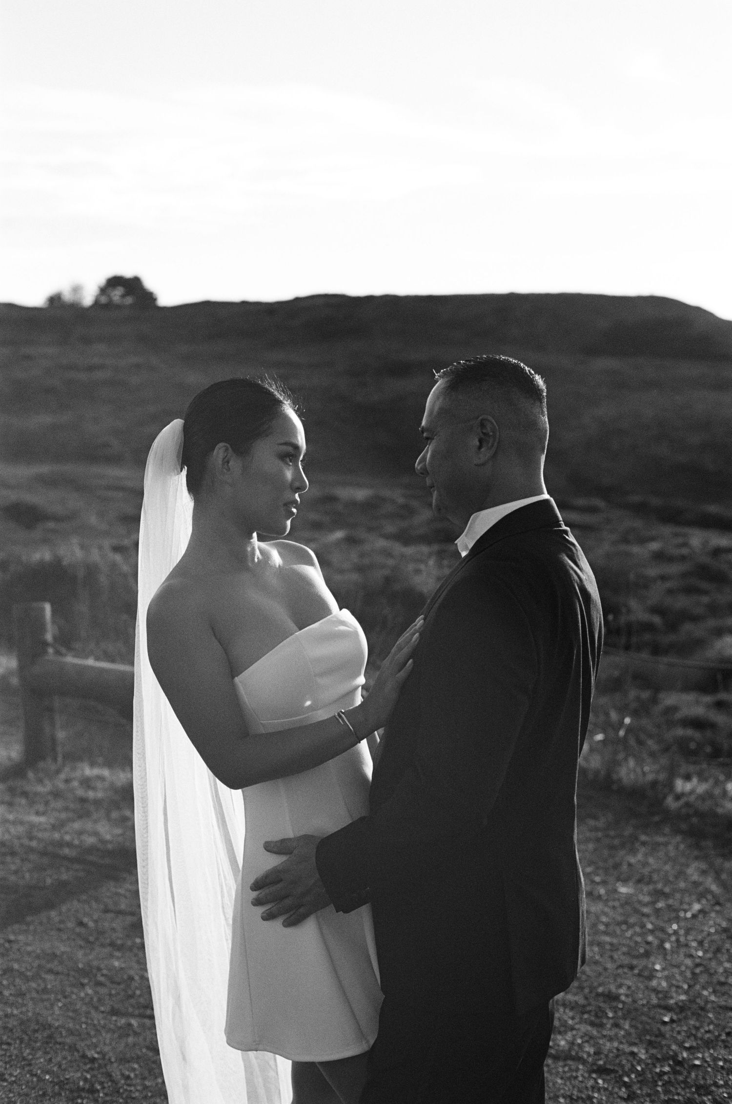 A black and white wedding portrait of a bride in a strapless dress and groom in a suit embracing outdoors.