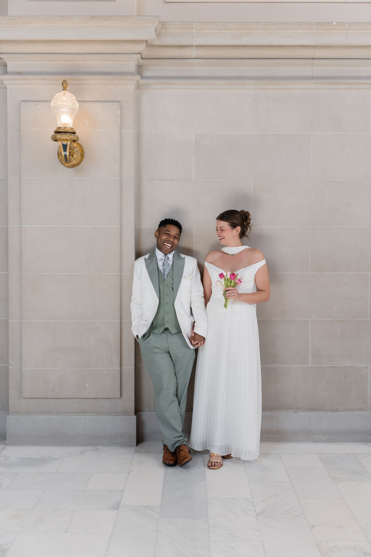 A couple in wedding attire poses against a light stone wall in a series of minimalist architectural wedding photos.