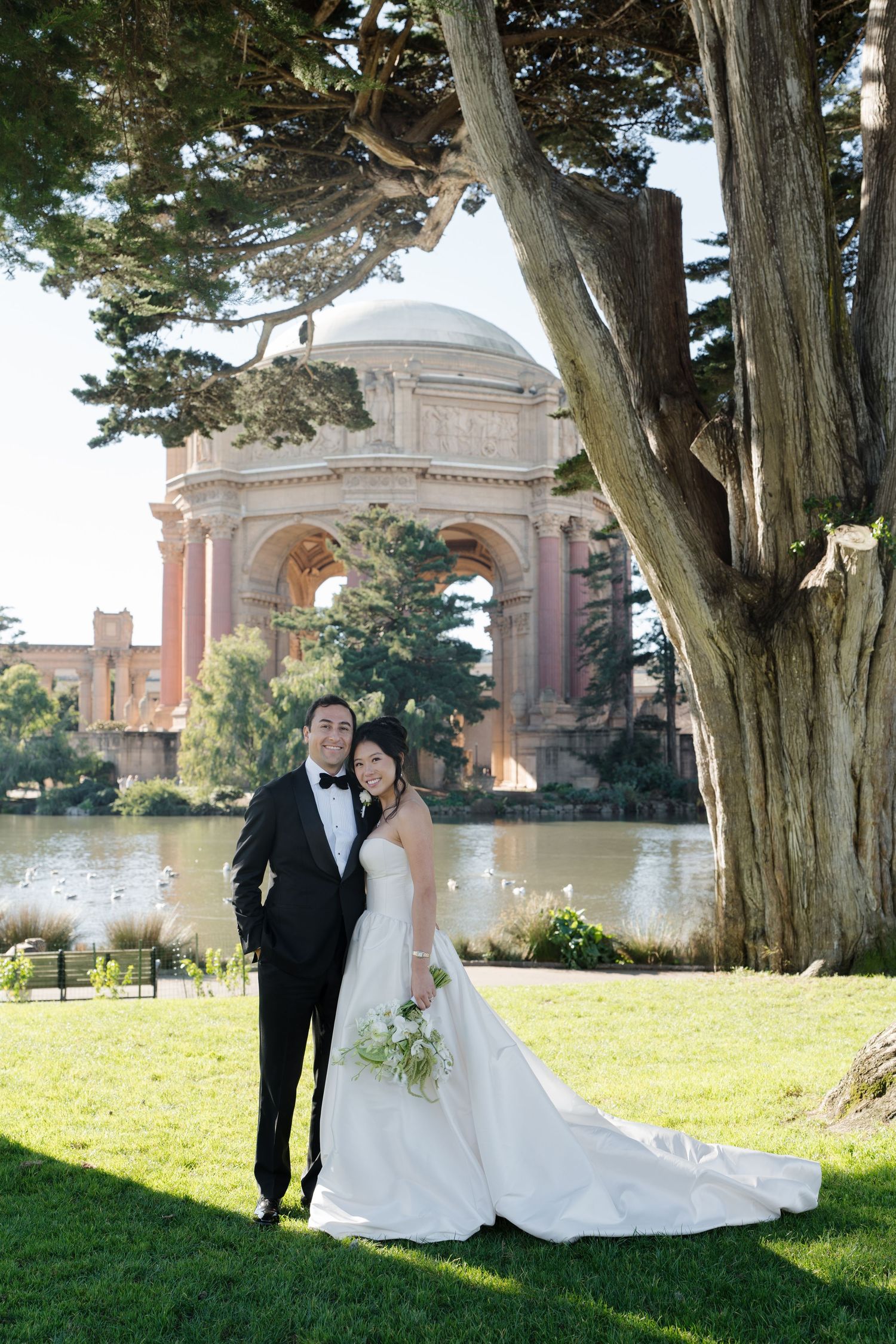 A couple poses for wedding photos in front of the Palace of Fine Arts in San Francisco on a sunny day.