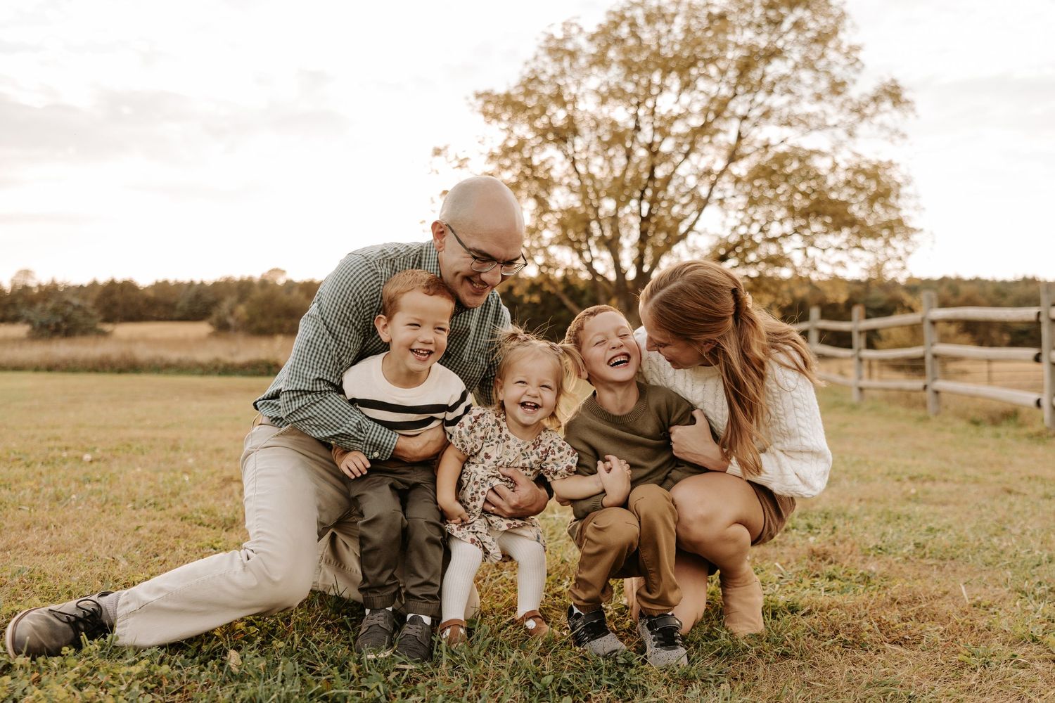 A loving family enjoys playful moments together in a golden field during sunset.