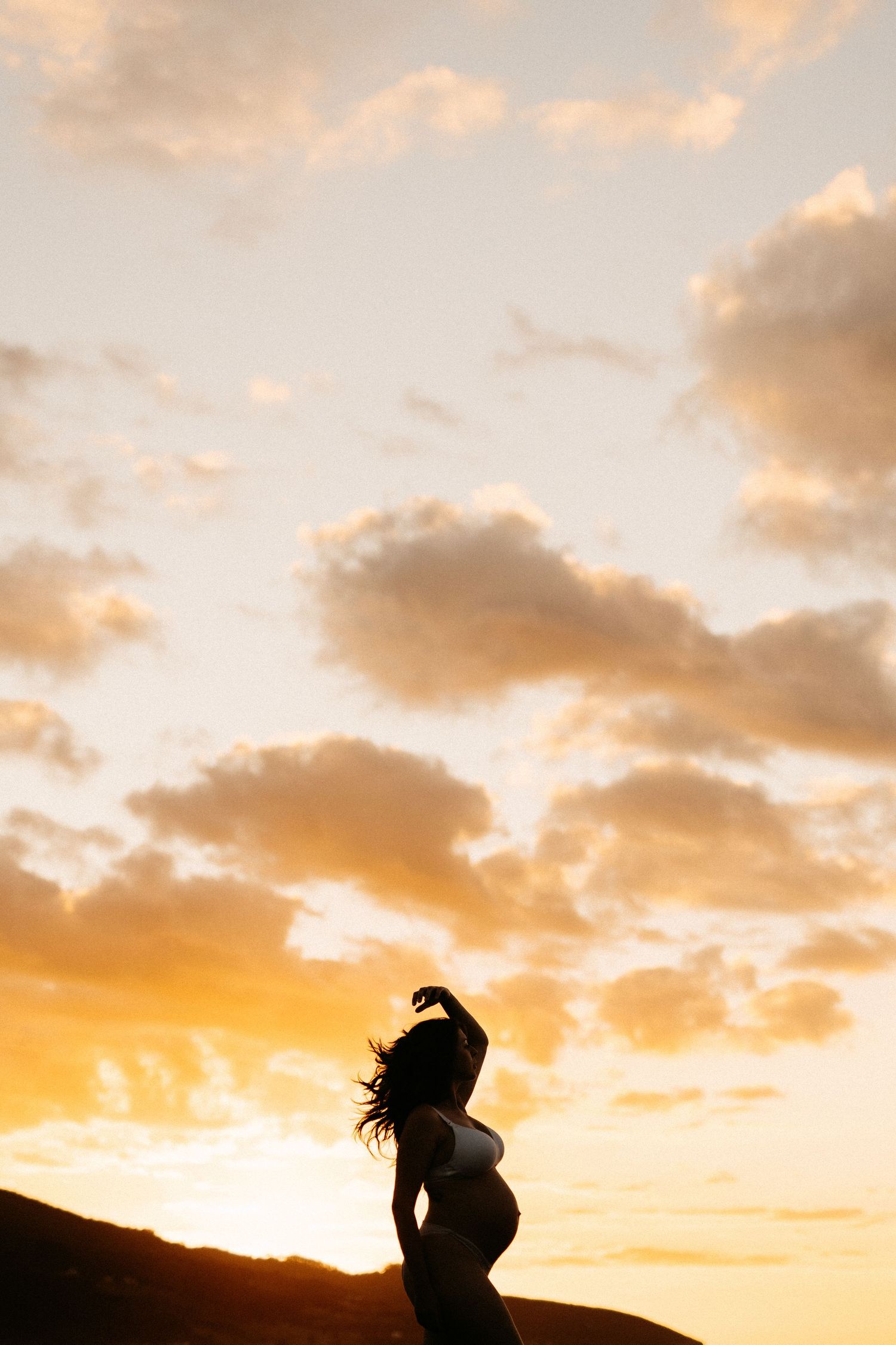 Silhouette of pregnant woman against dramatic sunset sky.
