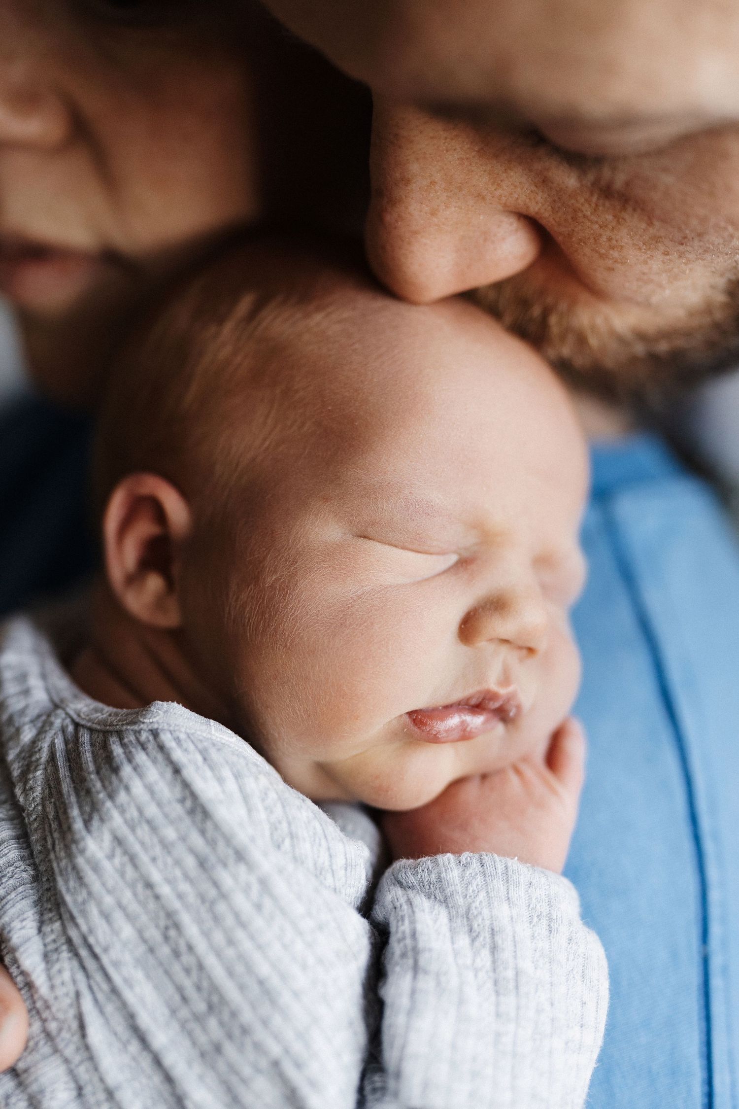 A sleeping newborn baby in a white knit sweater is held close and lovingly with gentle care.