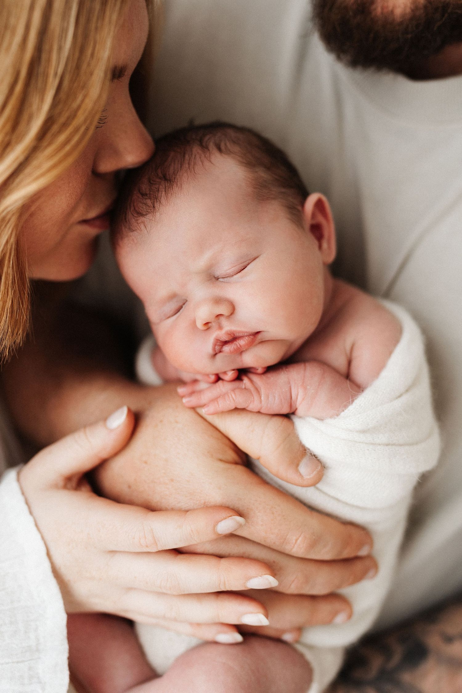 Tender close-up series showing a sleeping baby being lovingly held against soft white fabric.