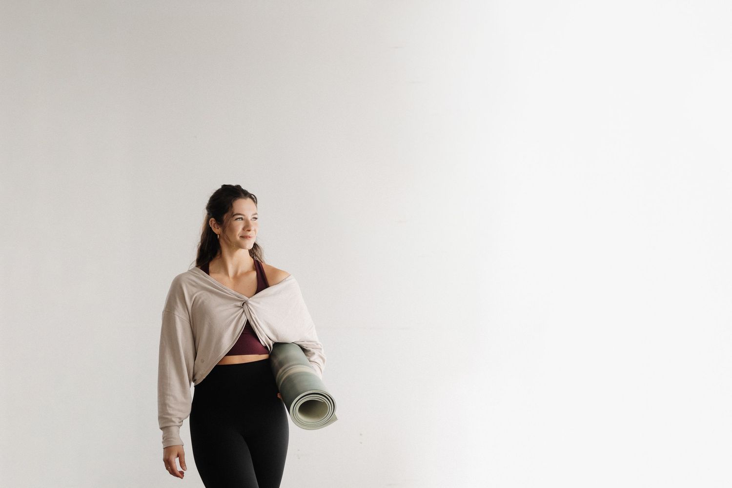 A pregnant woman in a black dress and beige cardigan poses against a white background during a maternity photoshoot.