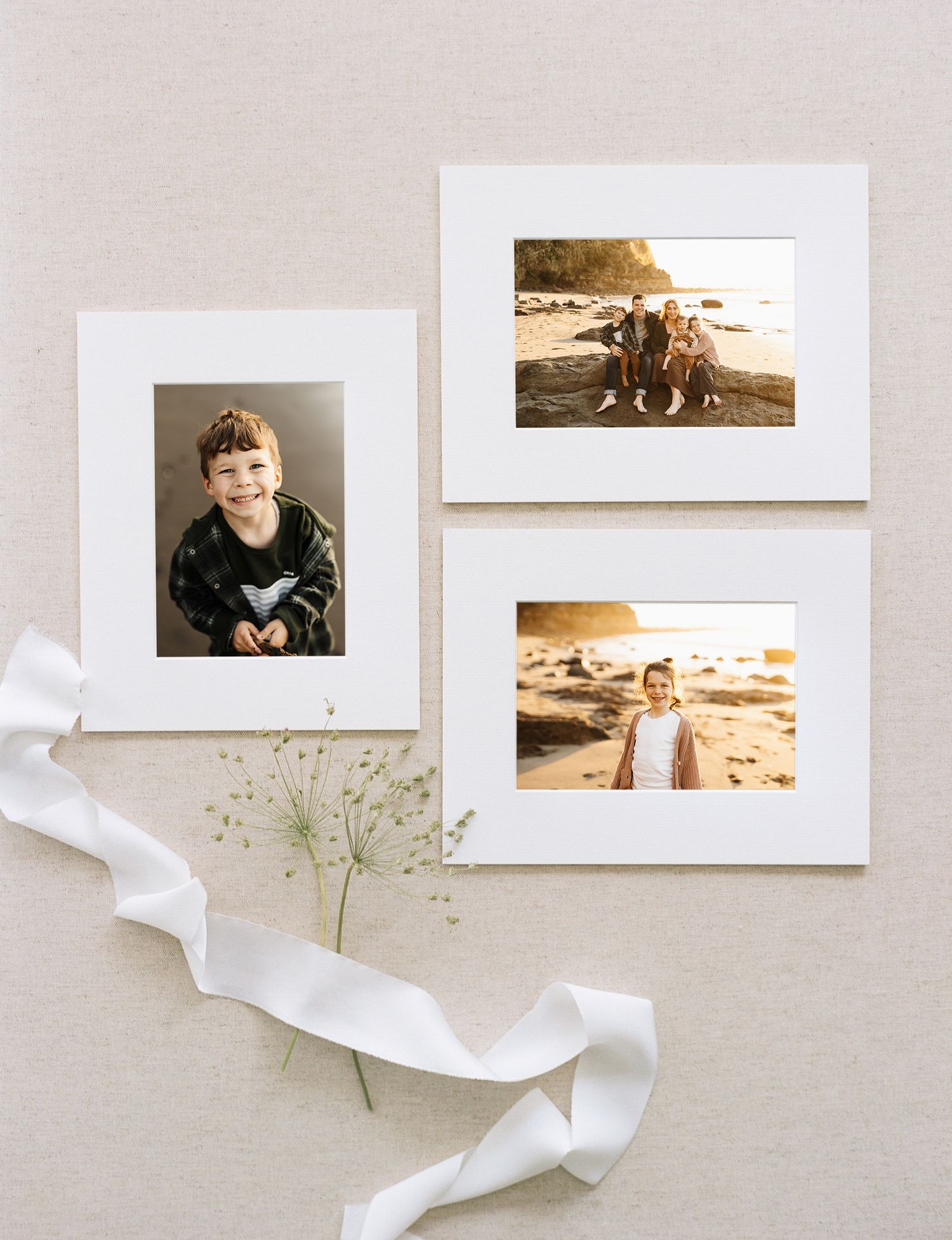 Artistic flat lay arrangement of white photo frames with silk ribbon and dried flowers on beige background.