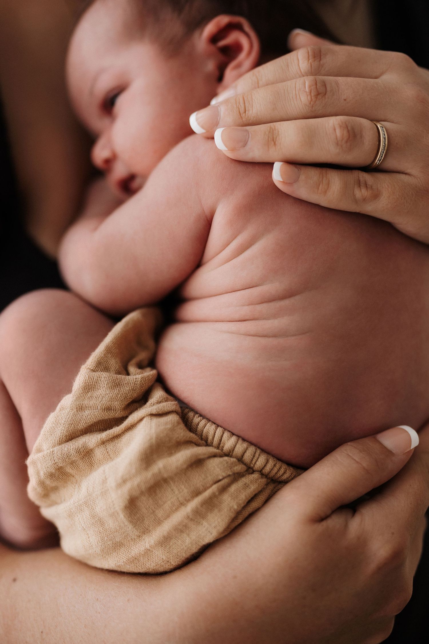 Gentle hands cradle a newborn baby wrapped in a soft beige blanket in a series of intimate close-up shots.