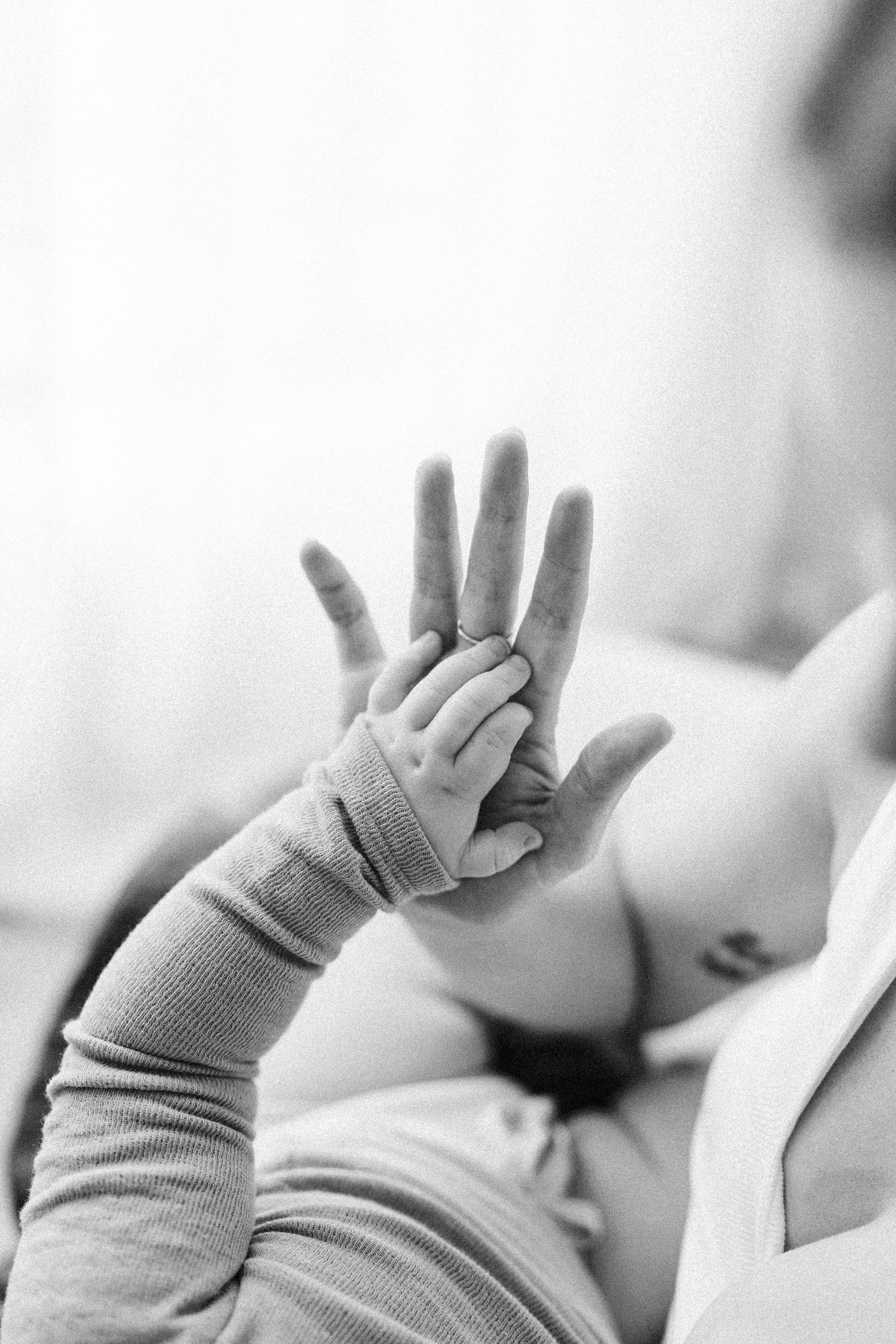 A tender black and white photograph of a tiny baby hand reaching up to touch an adult hand.