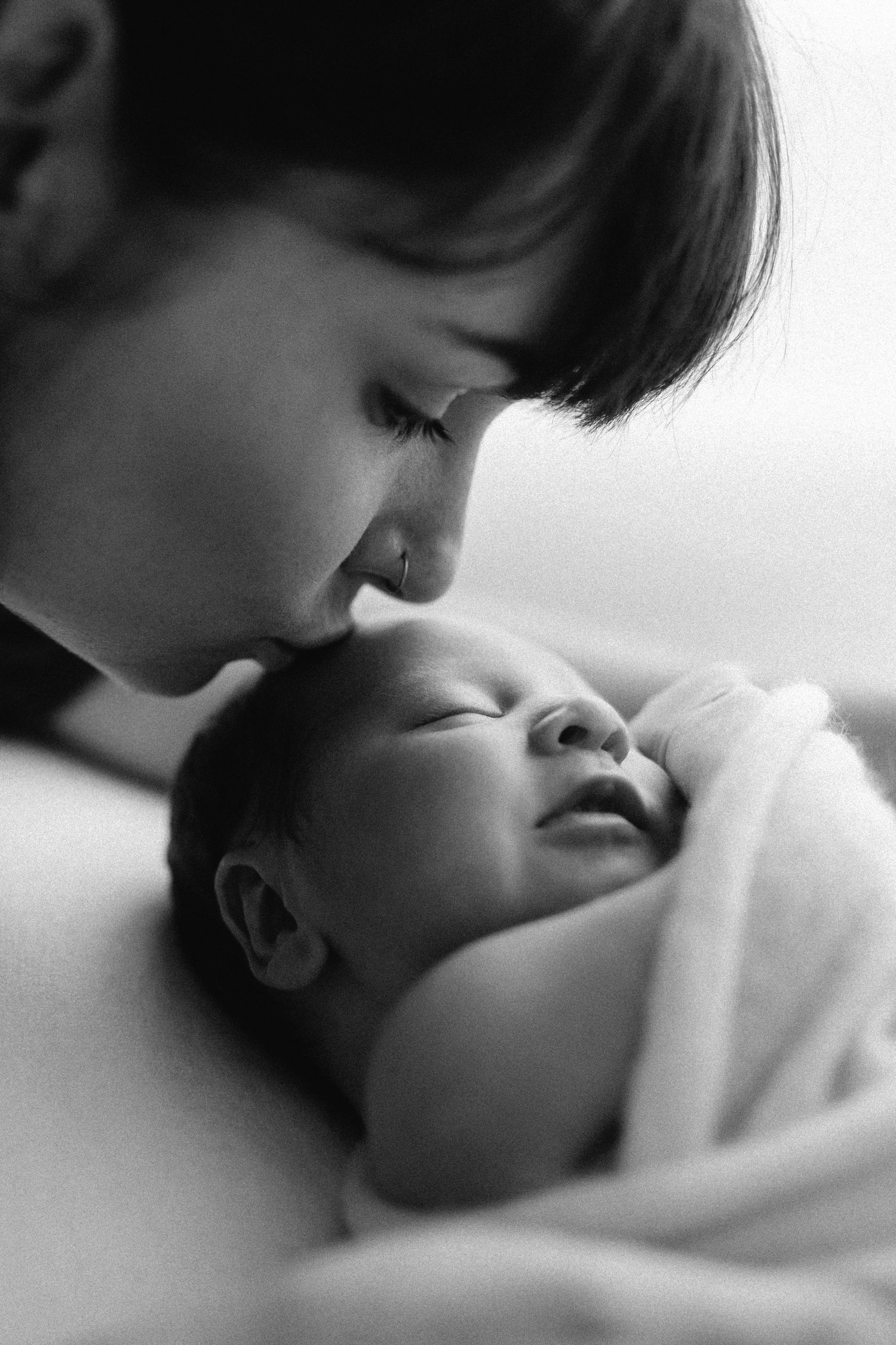 A tender black and white photo sequence showing a child leaning down to kiss a sleeping baby.