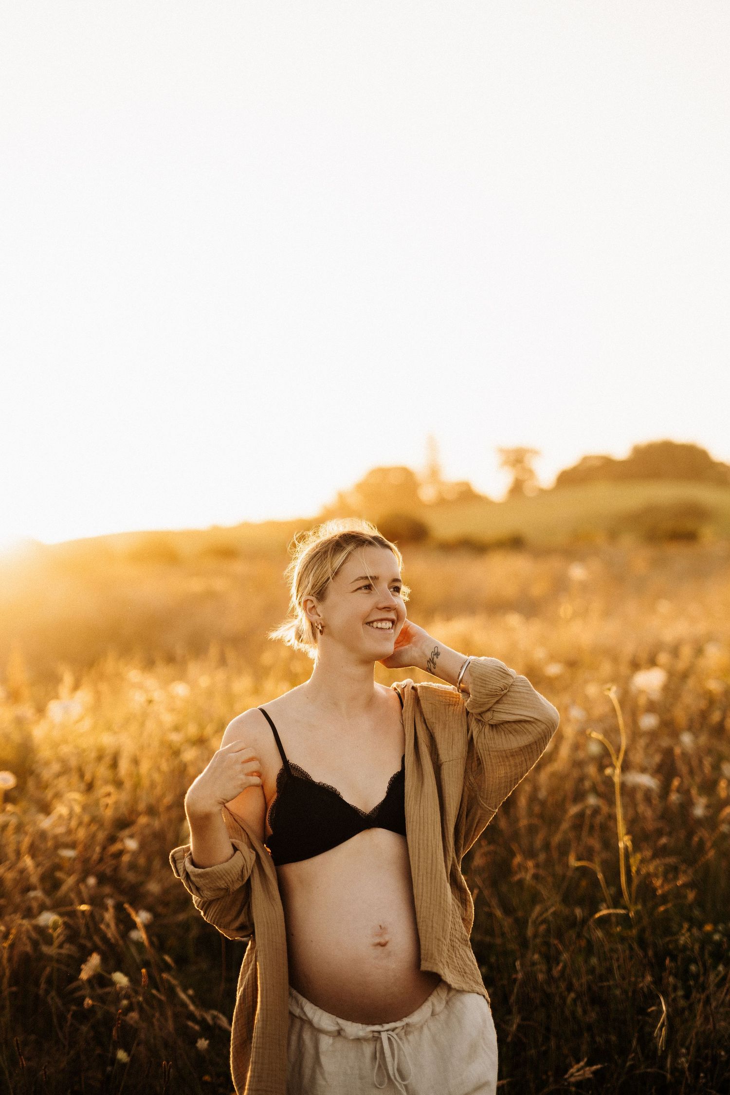 A person in a tan jacket poses in a golden field at sunset, creating a warm and ethereal atmosphere.