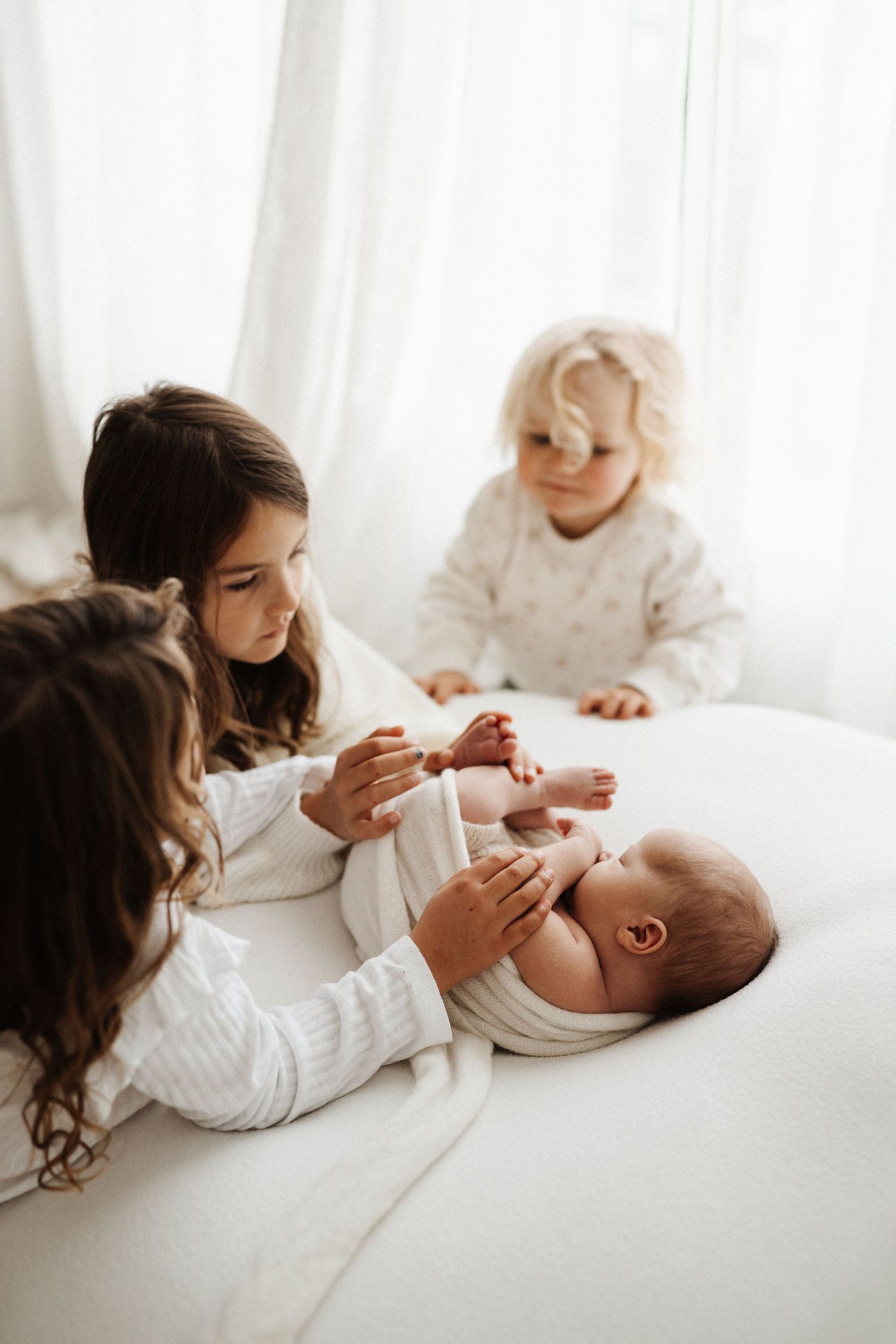 Sweet lifestyle photos of siblings bonding with their new baby on white bedding.
