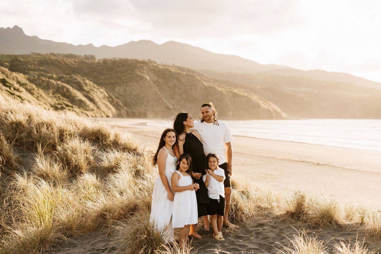 Family of four poses together on scenic coastal cliff at sunset.