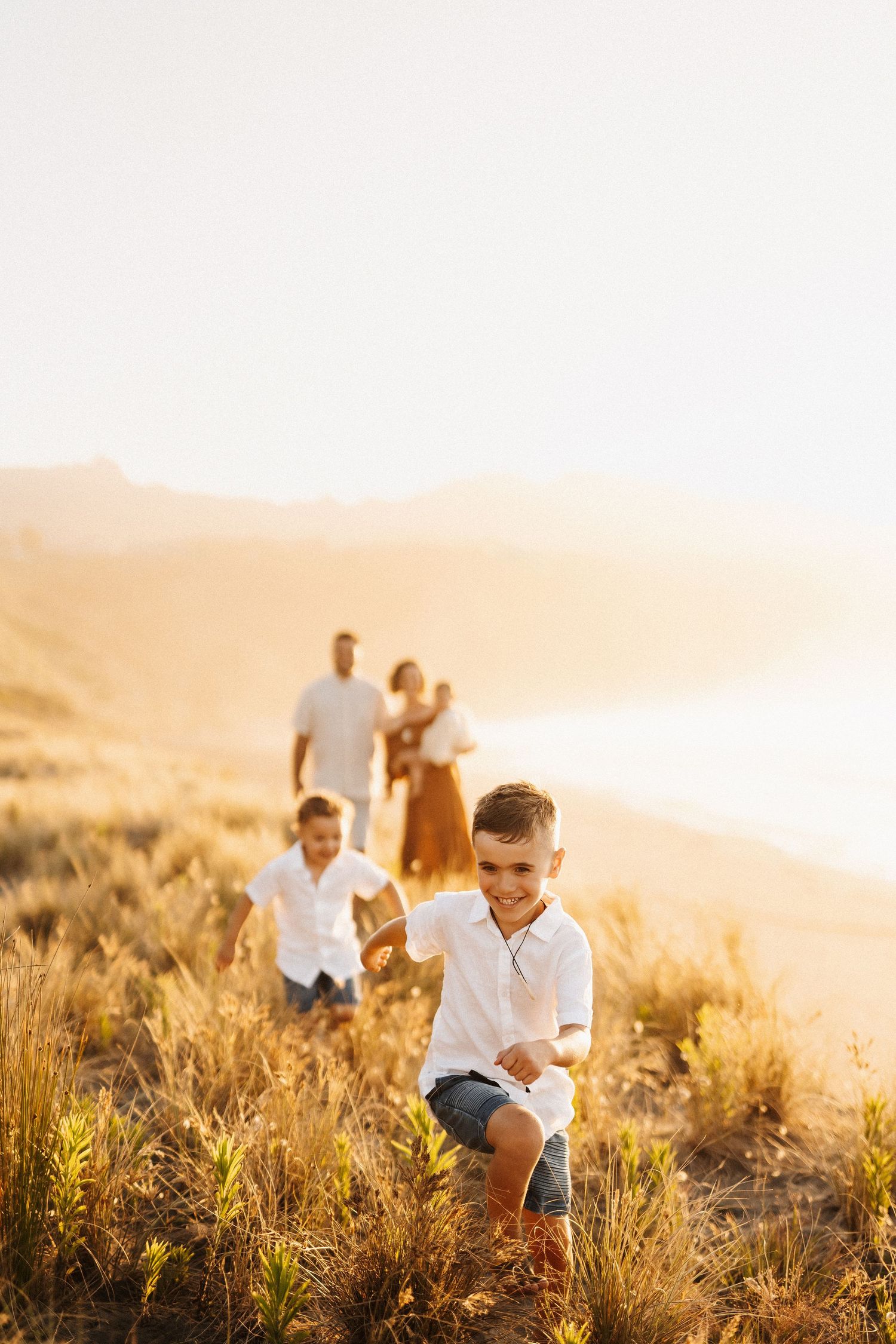Family walking through golden grass on coastal hillside at sunset.