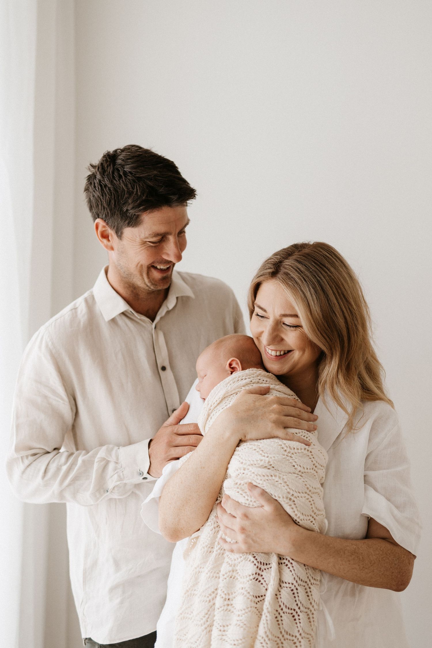 Joyful family moments captured in white as parents embrace their newborn.