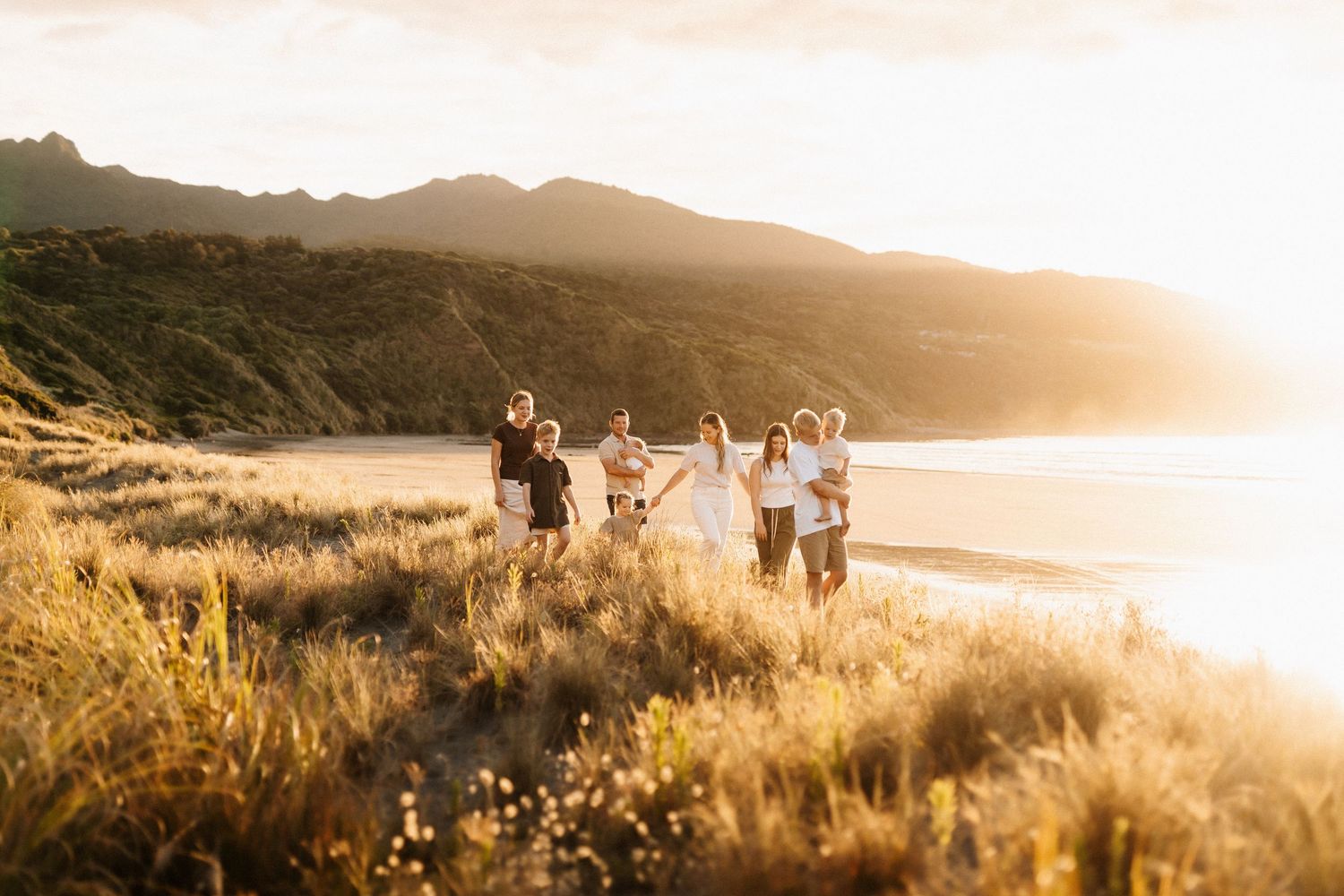 People running together through golden grass along a coastal mountain trail at sunset.
