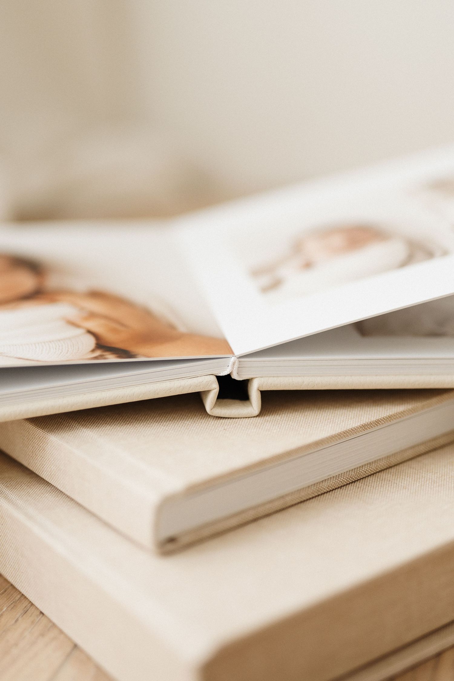 Close-up of stacked photo albums or books with cream colored covers on wooden surface.