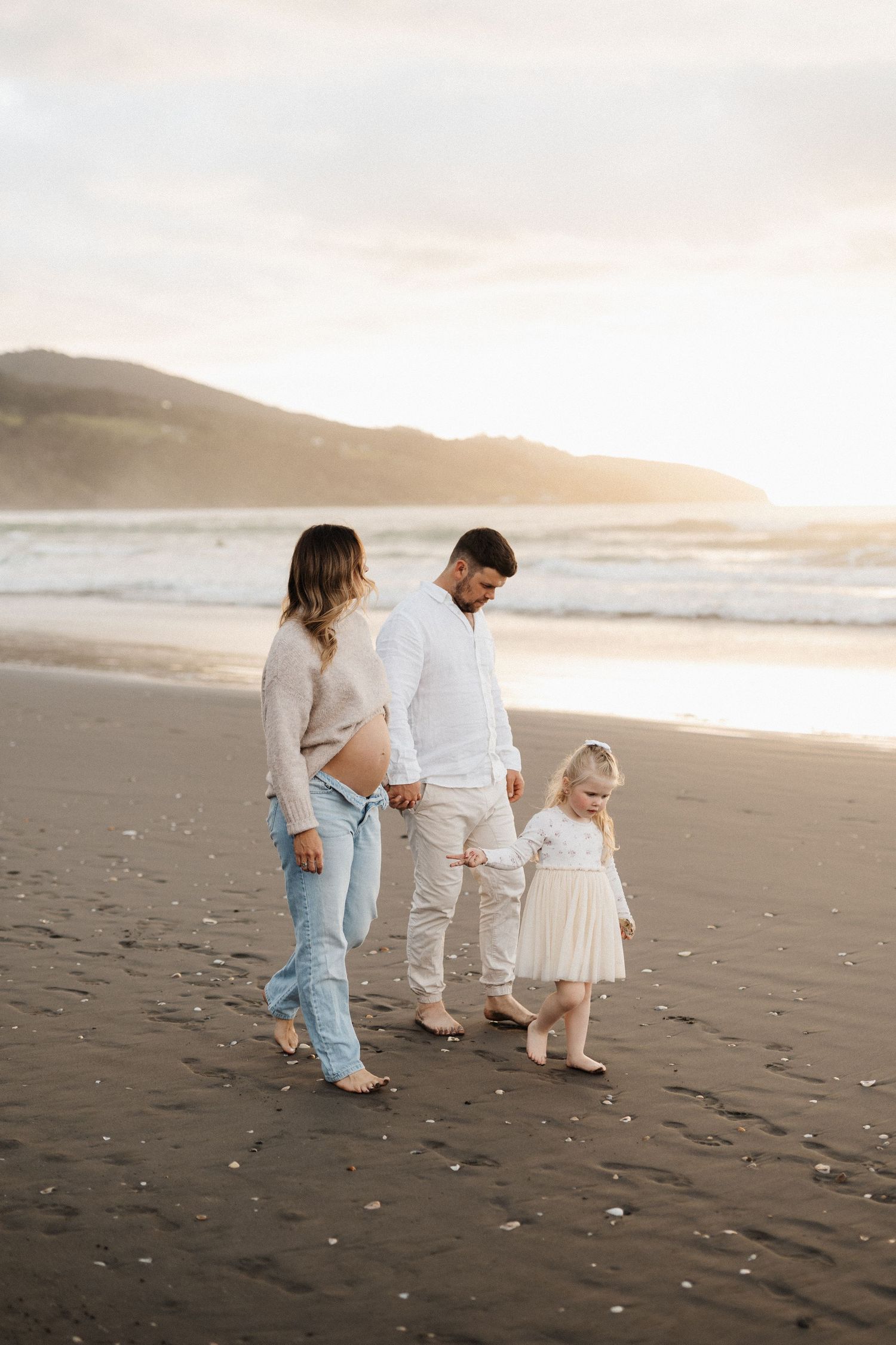 A family walks together on a scenic beach at sunset with mountains visible in the background.