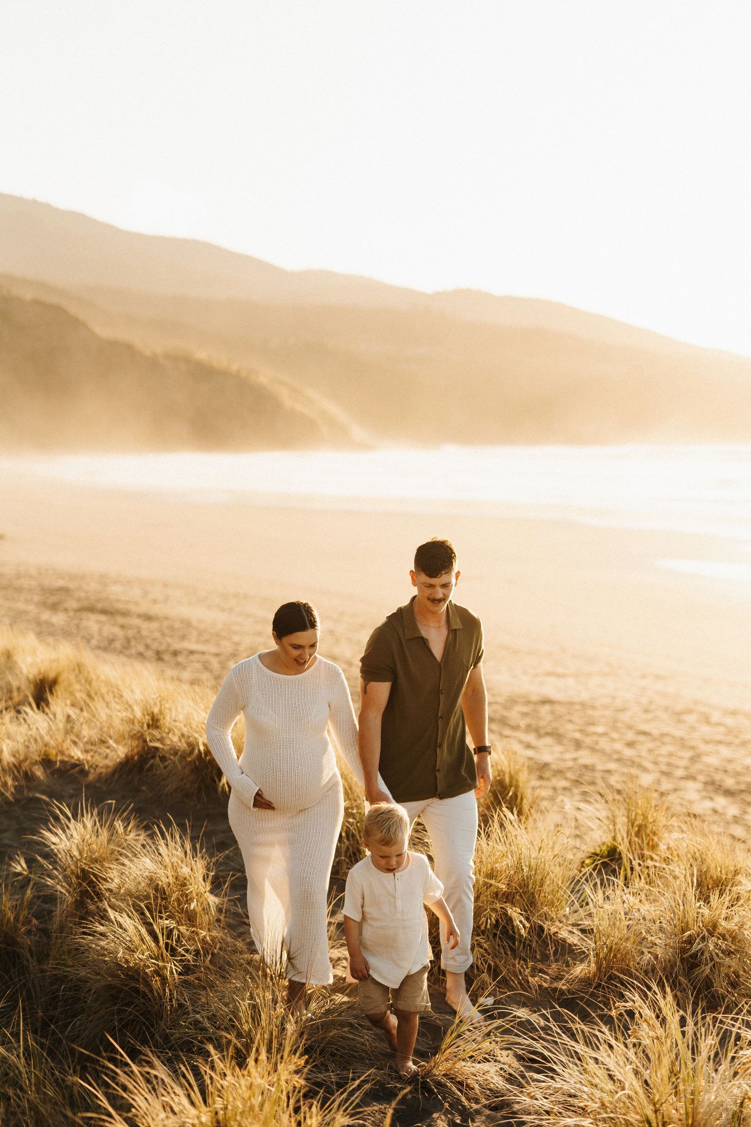 Family walks together through golden grass at sunset in a mountainous landscape with beautiful warm lighting.