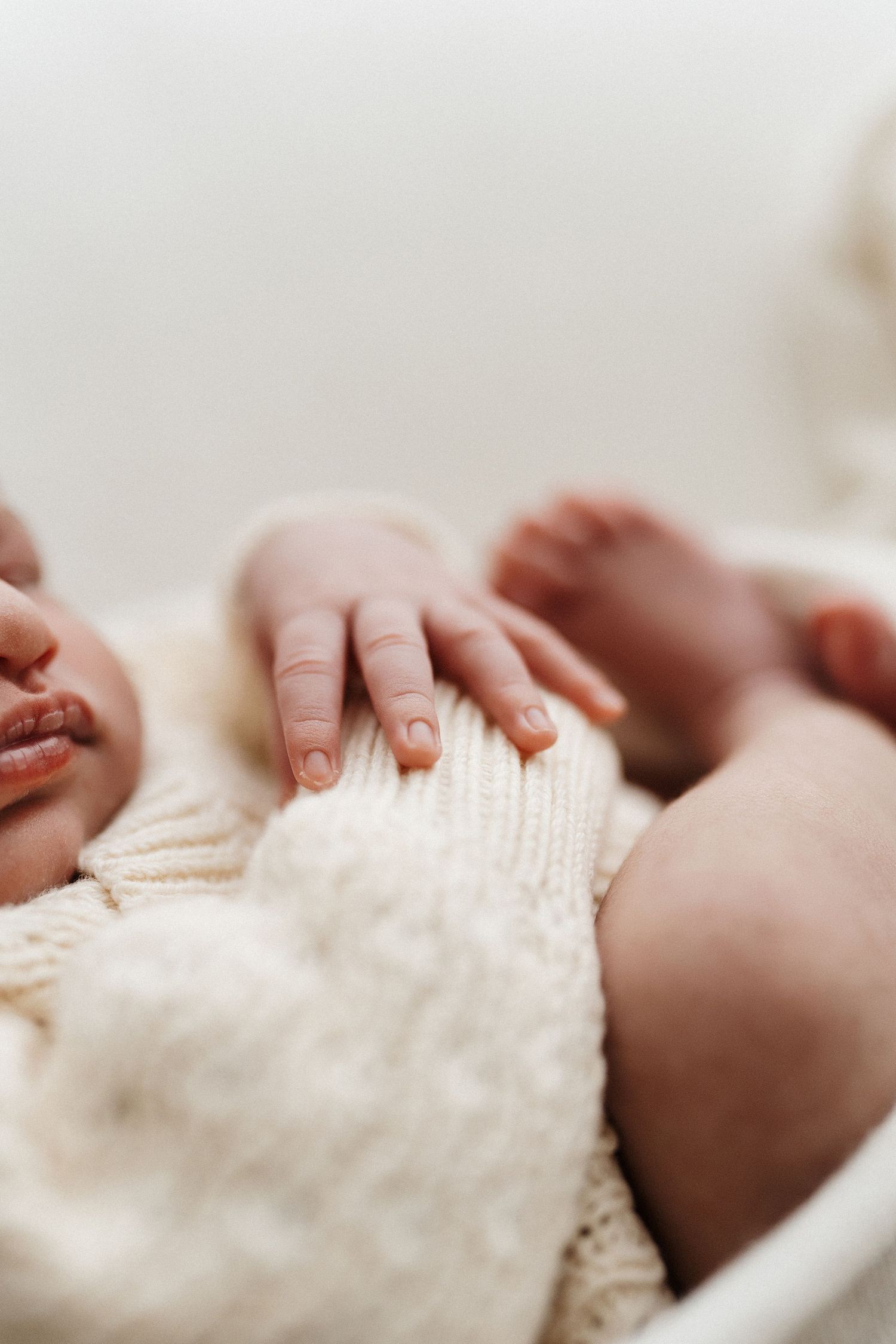 Close-up photo of small infant hands touching a soft knitted blanket or sweater in white.
