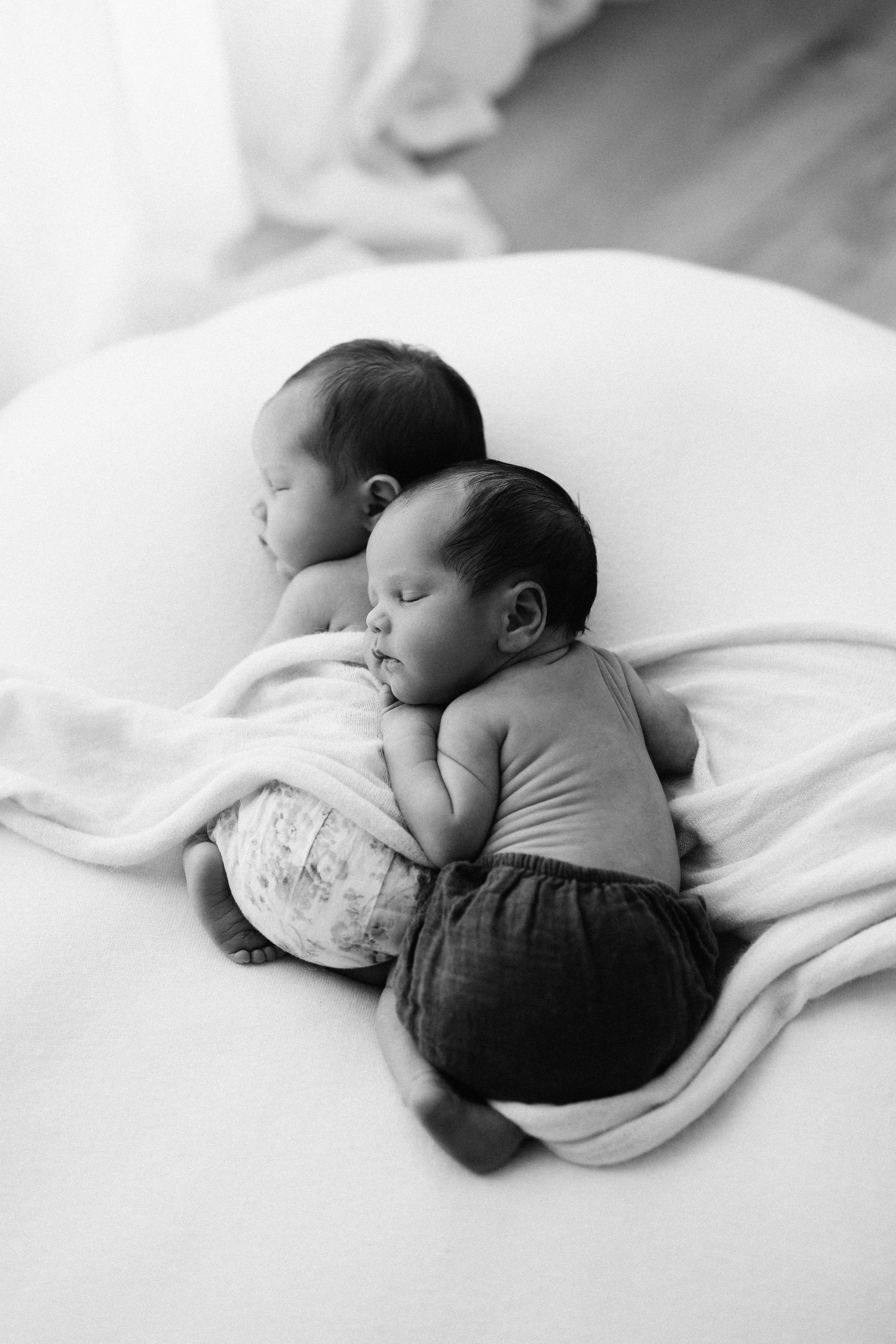 A peaceful black and white series showing a sleeping newborn baby nestled in soft white bedding.