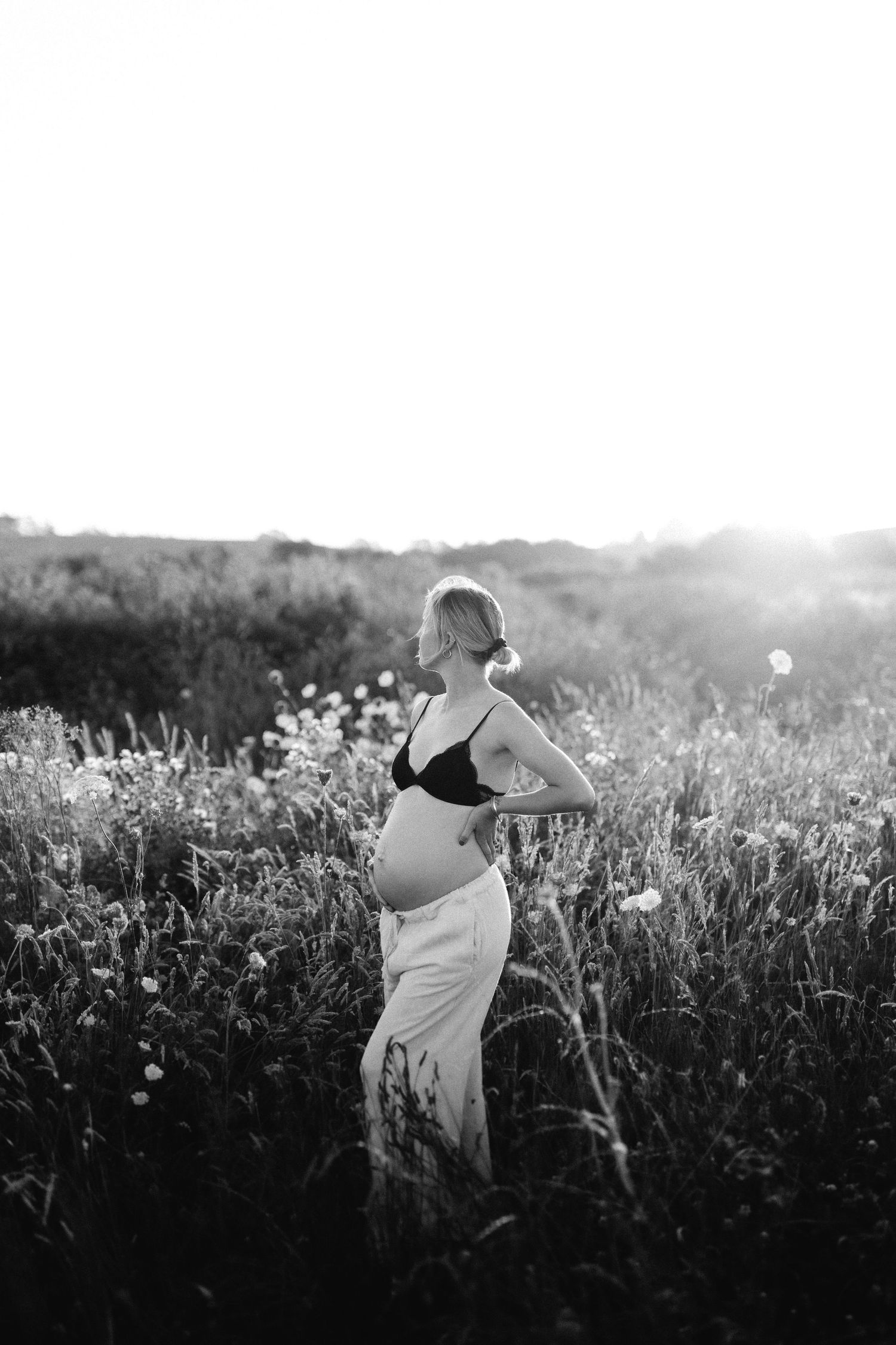 A person in a white dress walks through a misty meadow of tall wildflowers at sunset.