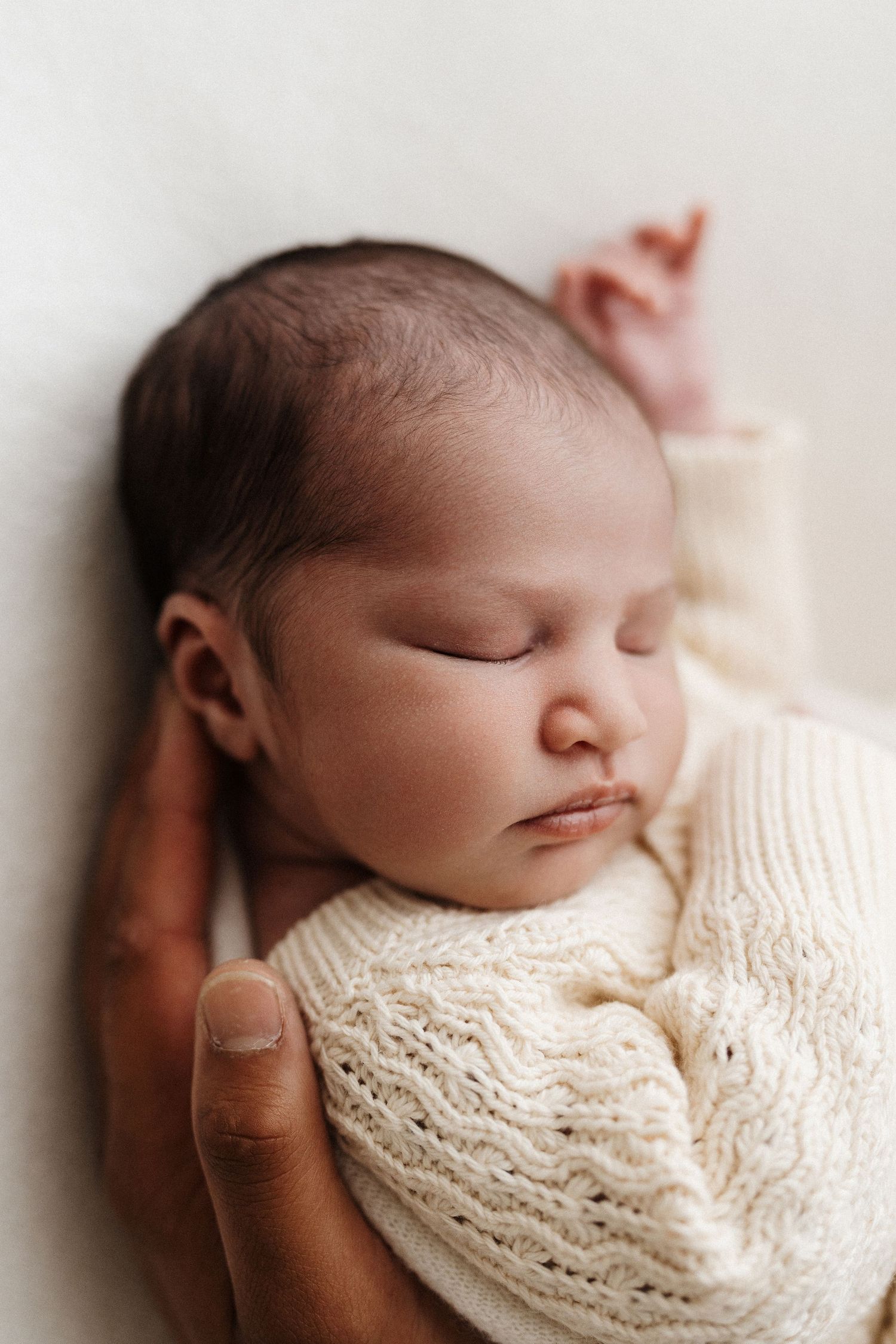 Sweet newborn baby peacefully resting, wrapped in delicate ivory lace fabric in a gentle natural light setting.