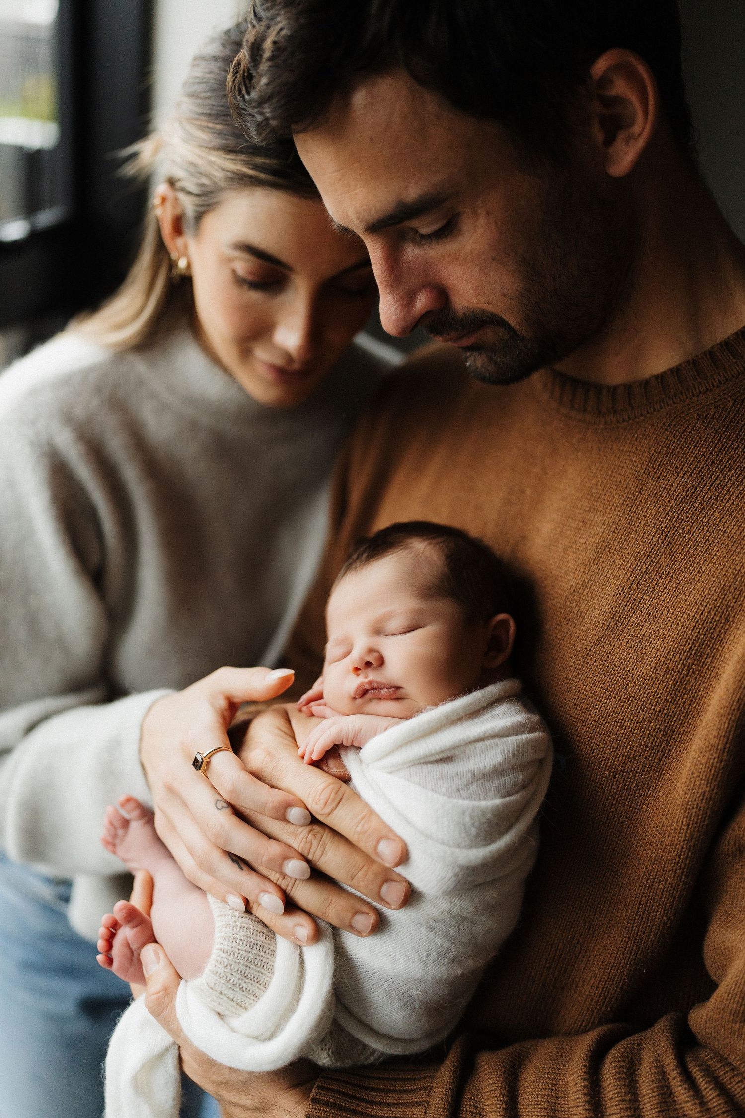 A sequence of five intimate moments showing a parent in a brown sweater tenderly holding and bonding with a newborn.