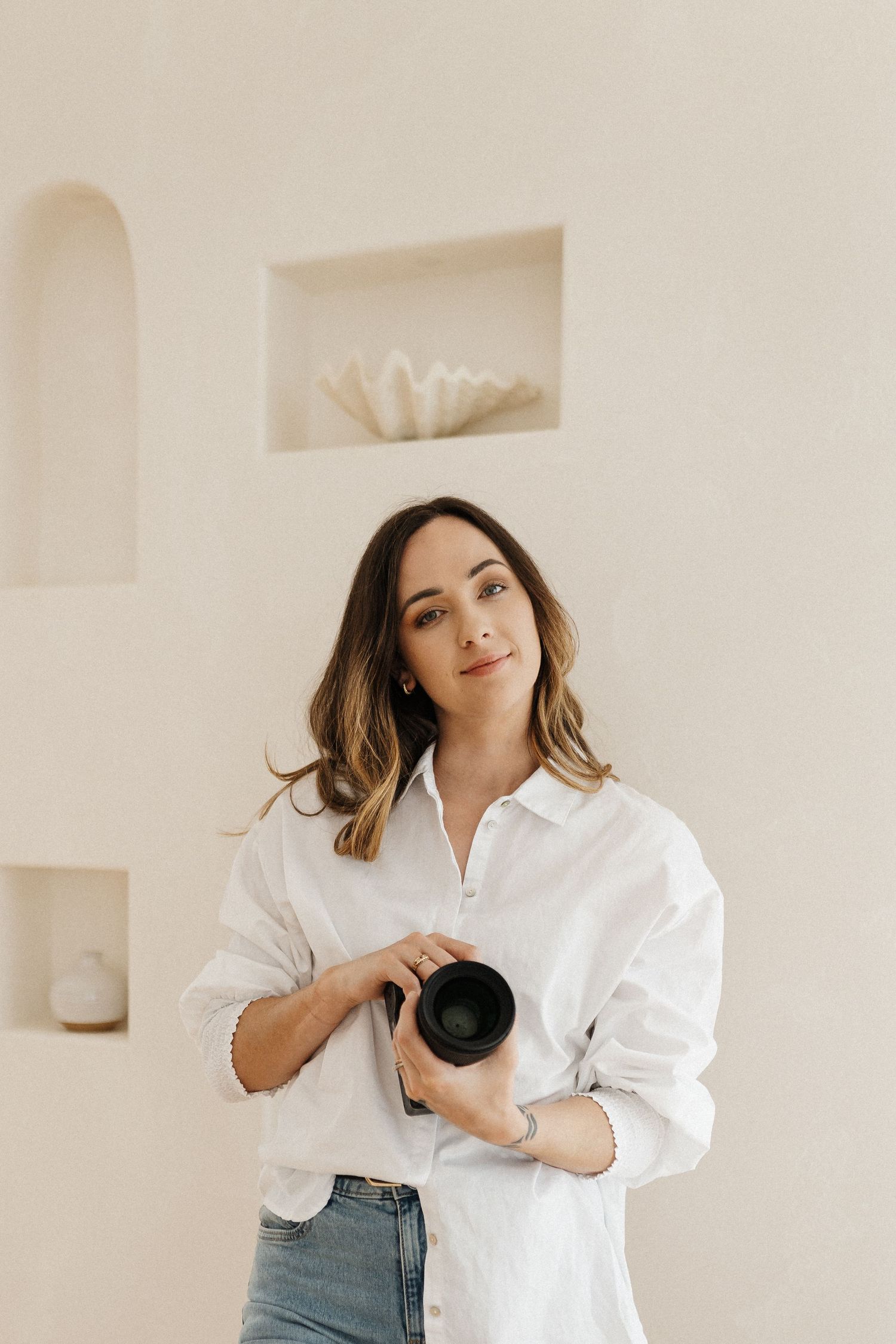 Person in white button-down shirt and jeans poses against white wall in minimalist photo series.