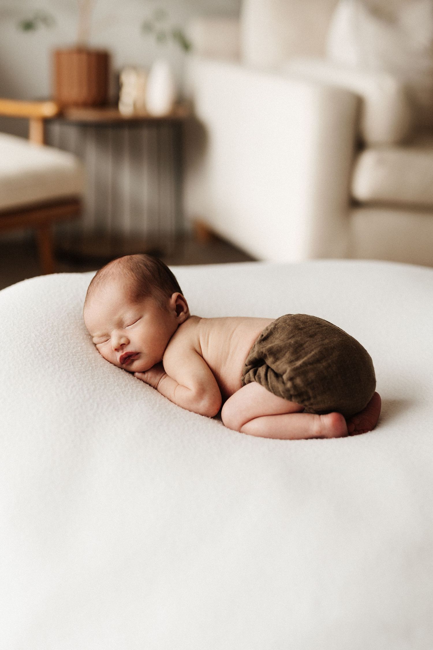 Peaceful newborn baby sleeping on soft white bedding in natural window light.