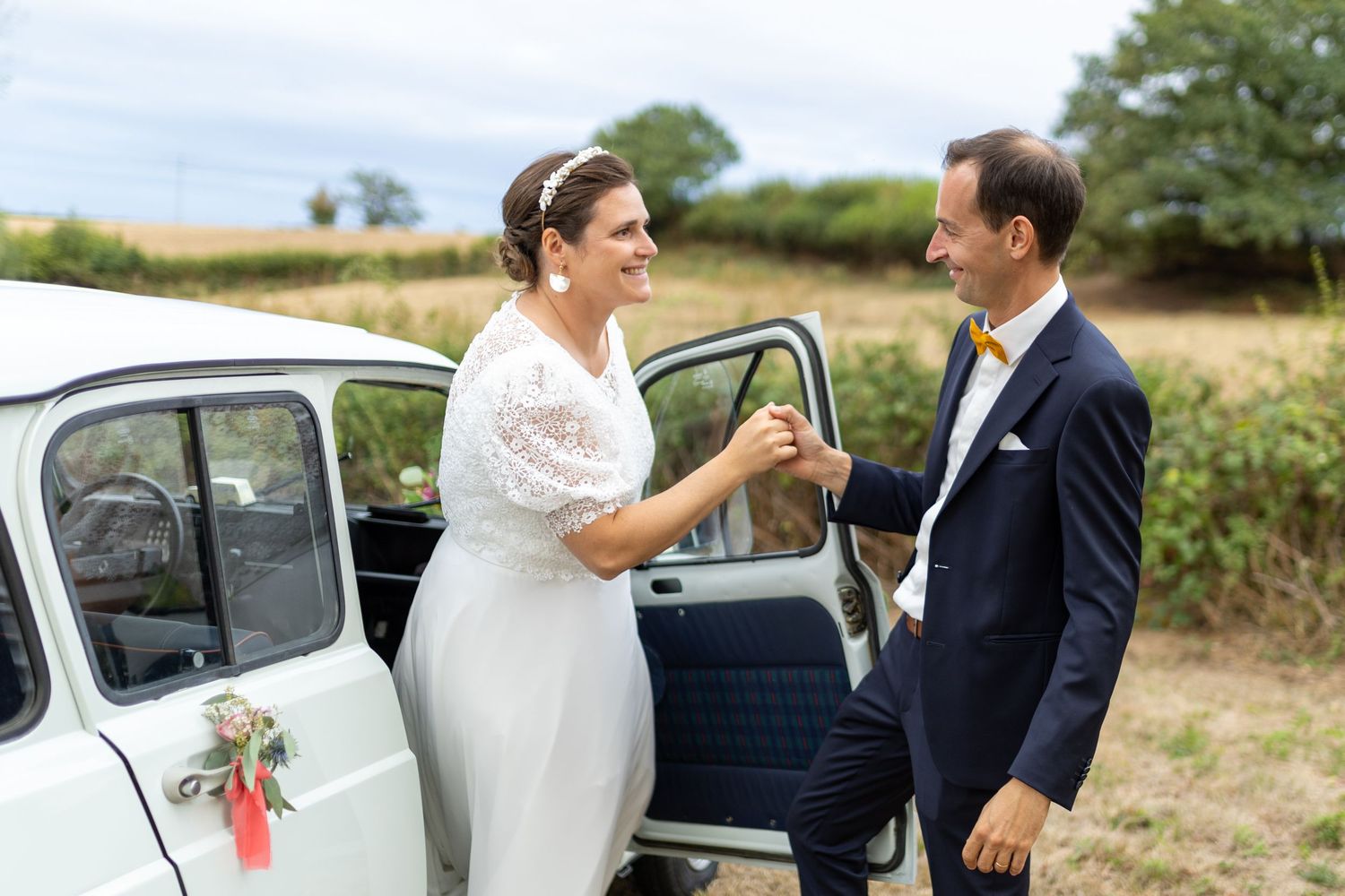 Mariée descendant d'une voiture ancienne accompagnée du marié
