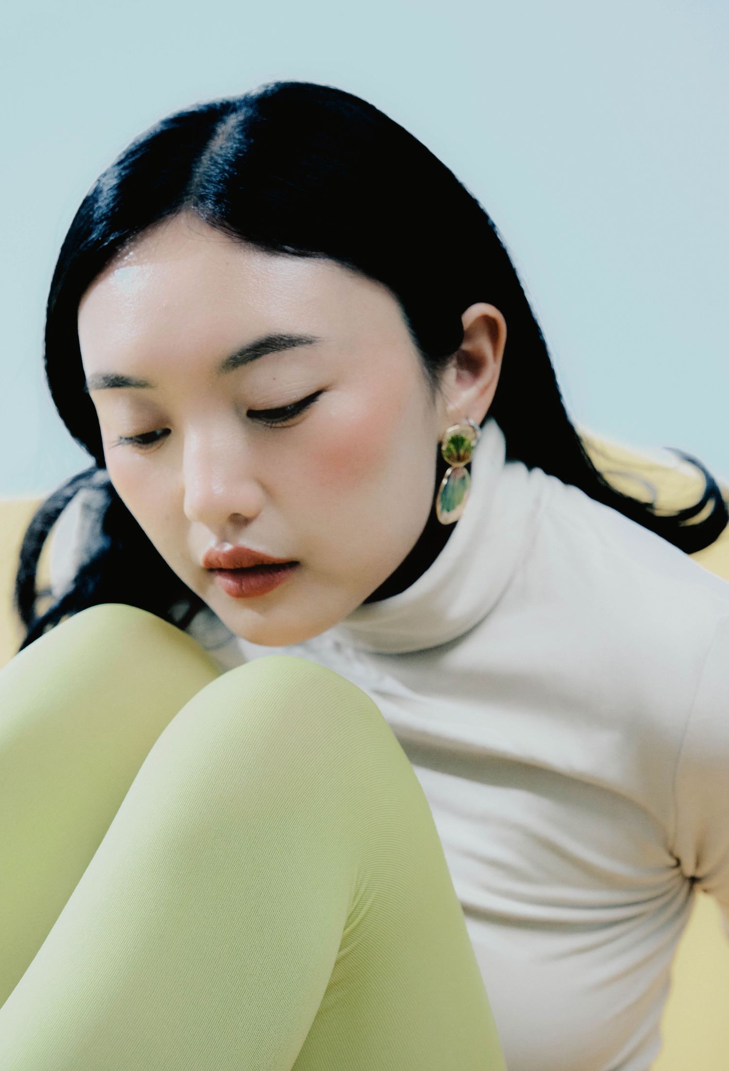 35mm film portrait of a woman with eyes closed, wearing a cream turtleneck and yellow earrings, pastel color palette