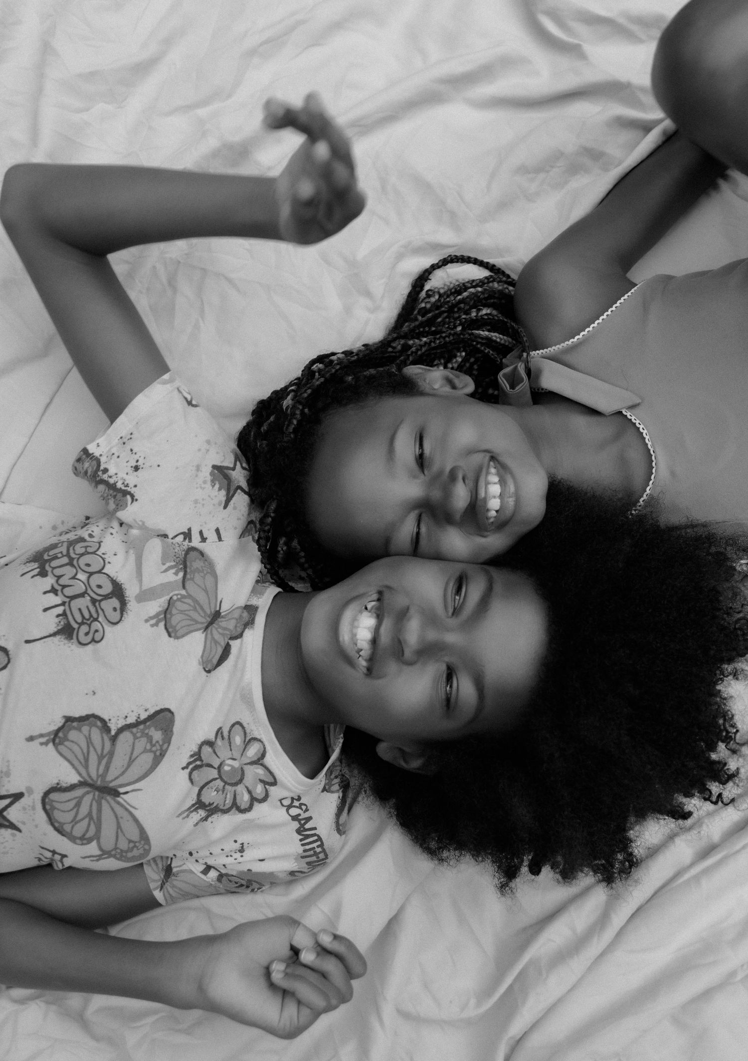 Two sisters lying head to head on a white sheet, laughing, in a black and white family photo