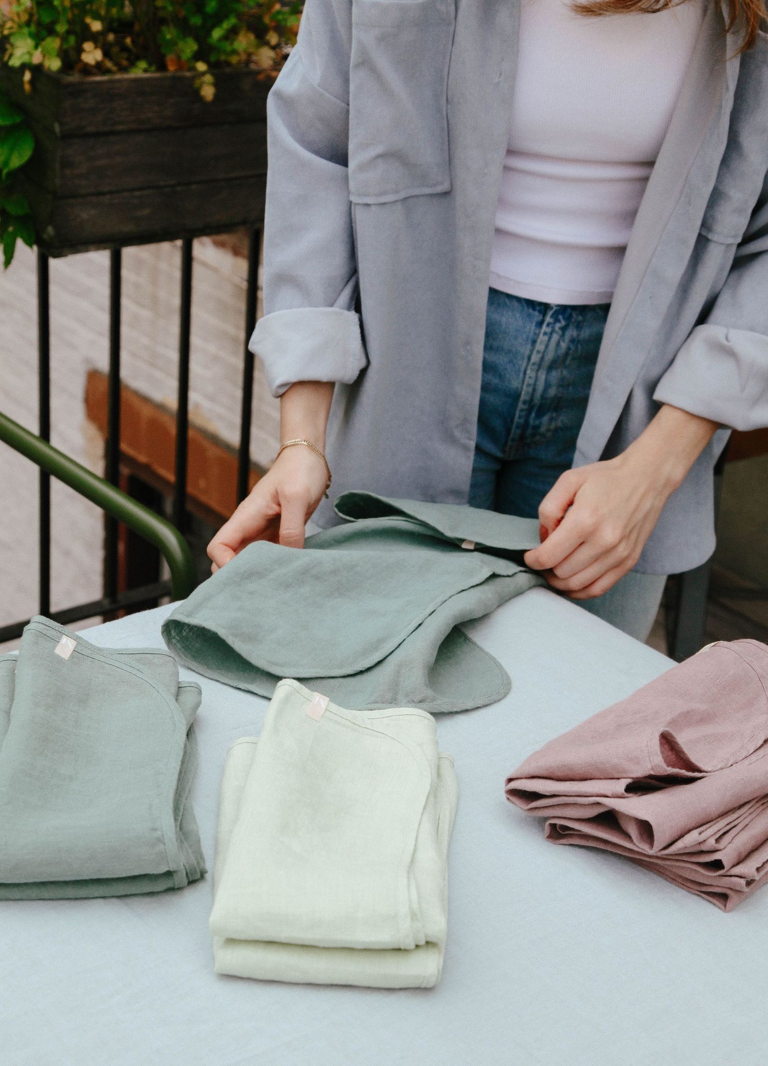 Woman folding kitchen linen napkins in sage, cream, and pink on an outdoor table