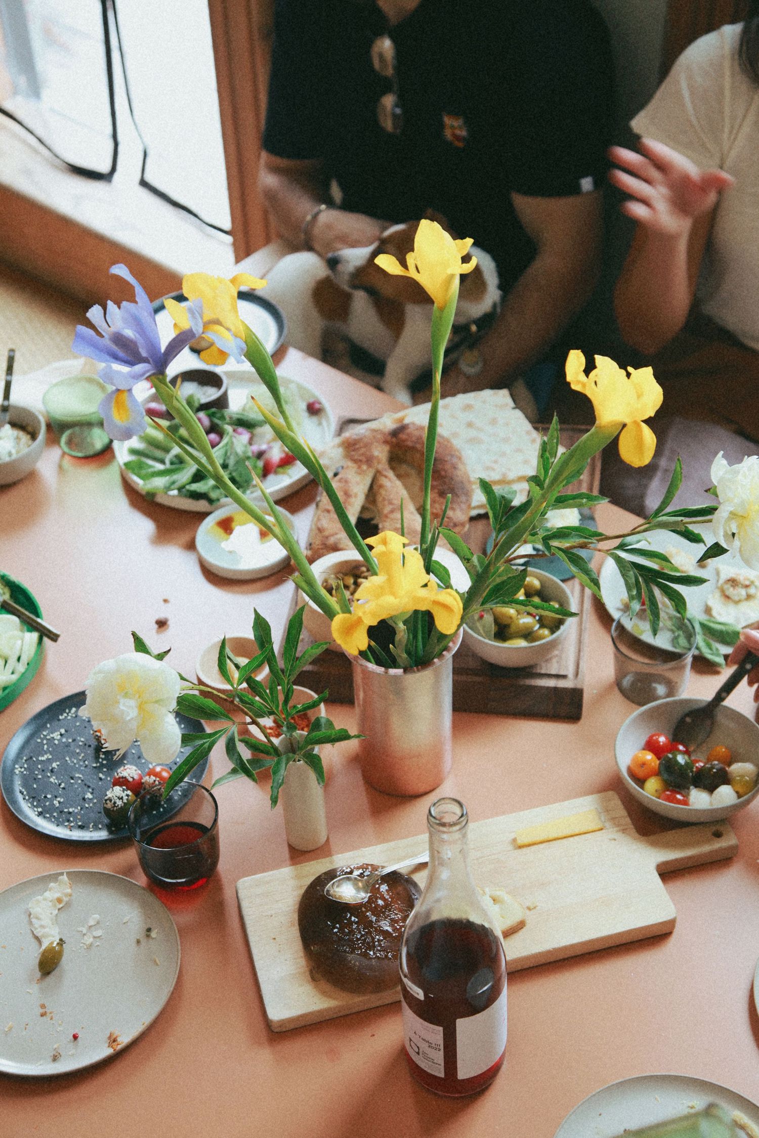 Documentary-style photo of an NYC dinner party table with irises, shared plates, bread, and wine
