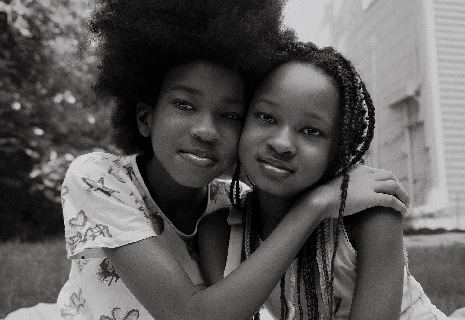 Black and white portrait of two sisters cheek to cheek, smiling softly in the backyard