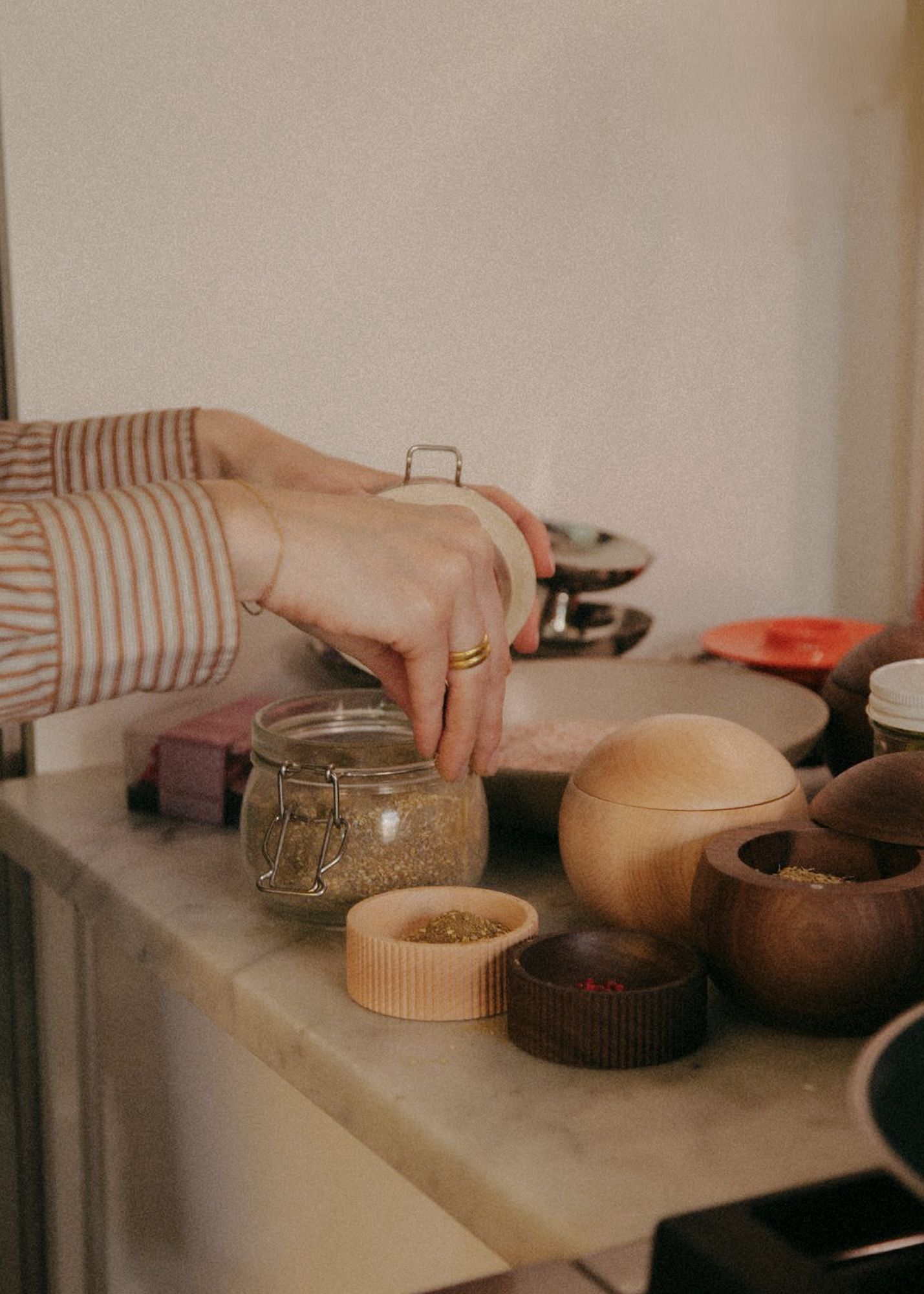 Hands opening a glass spice jar on a marble counter beside wooden bowls, kitchenware lifestyle photography