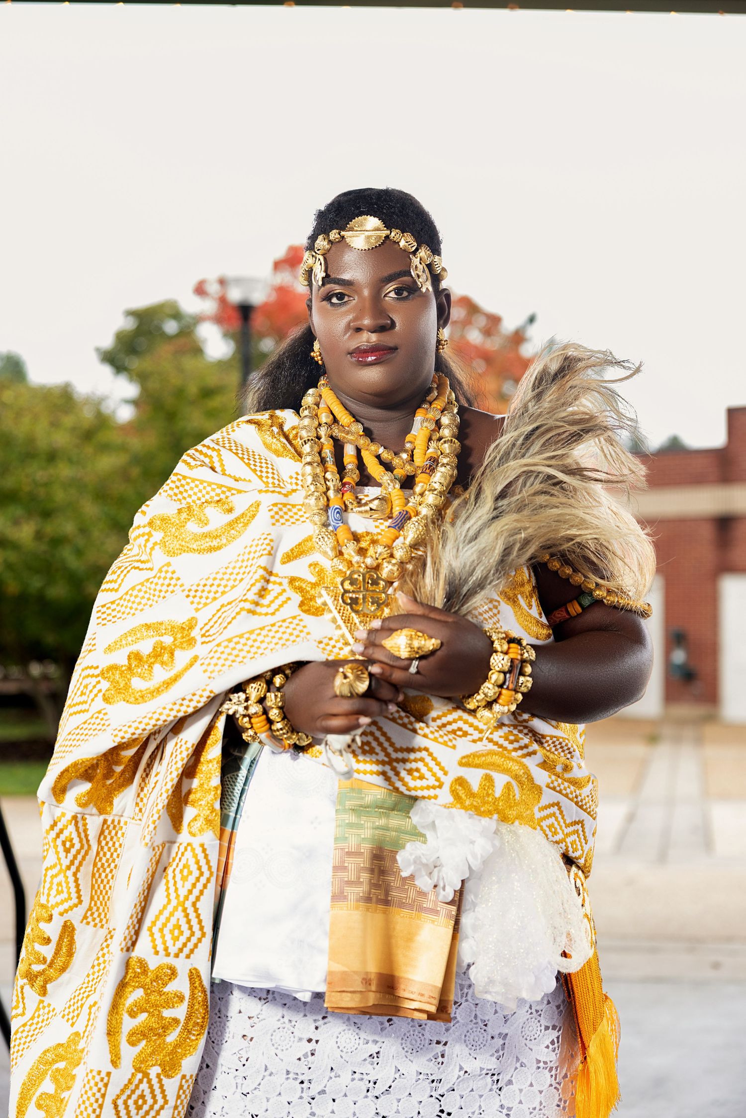 Portrait of a person wearing traditional Ghanaian attire in white and gold, photographed outdoors by Horlali Captures.