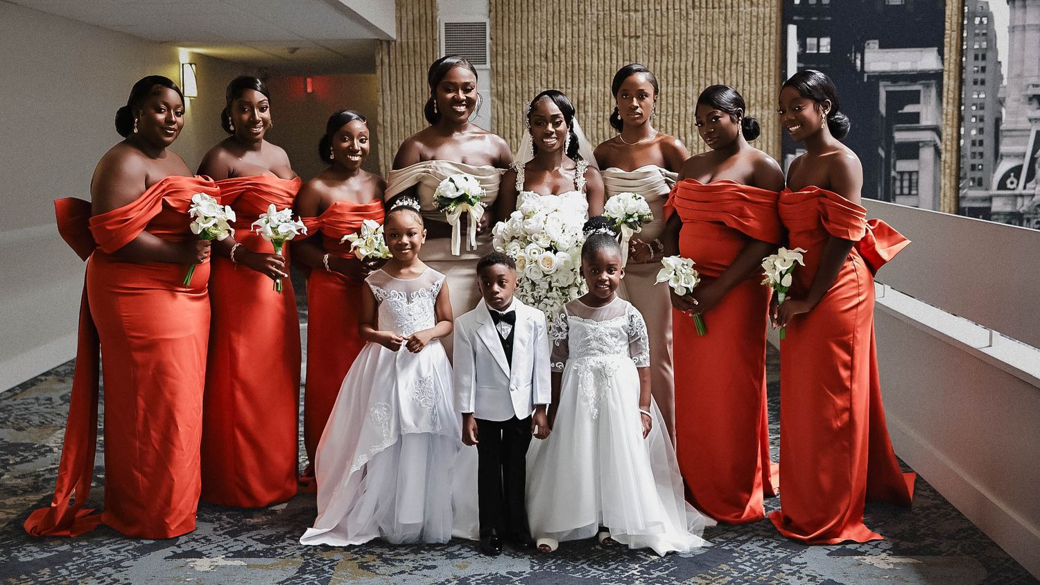 Bride in a white wedding gown surrounded by bridesmaids in burnt-orange dresses holding bouquets.