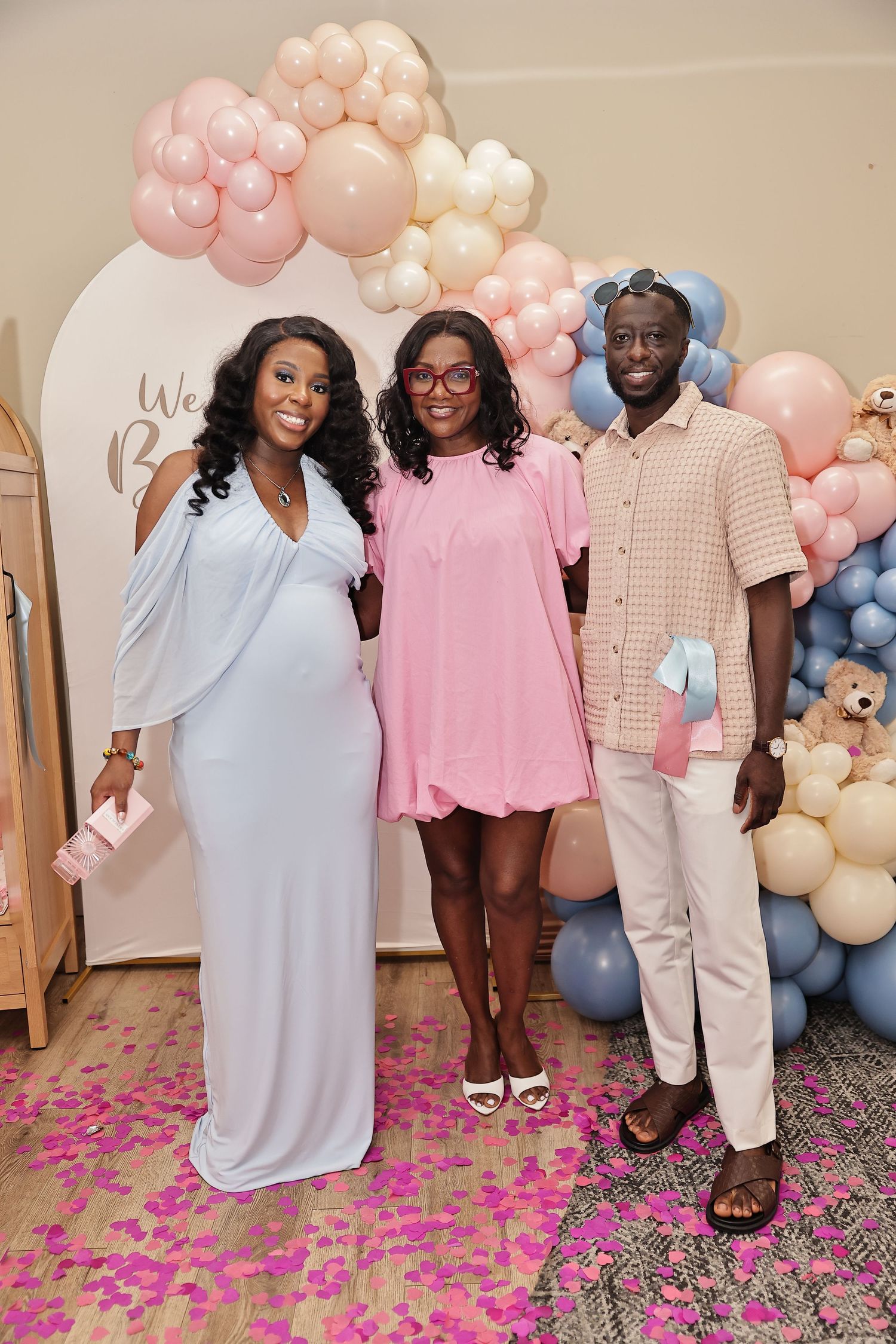Family posing together in front of a pink, cream, and blue balloon arch at a celebration.
