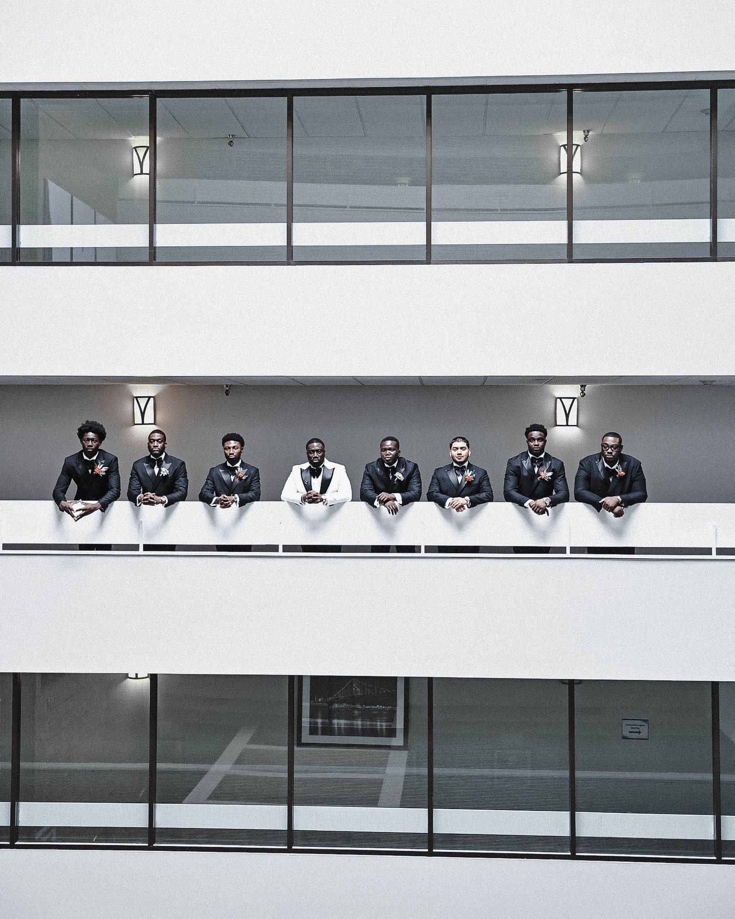 Groom and groomsmen posing together along the balcony of a modern building.